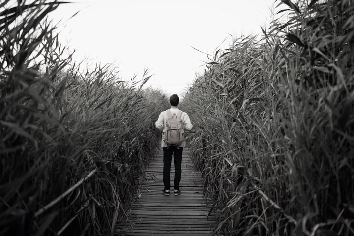 A man with a backpack walks through tall grass.