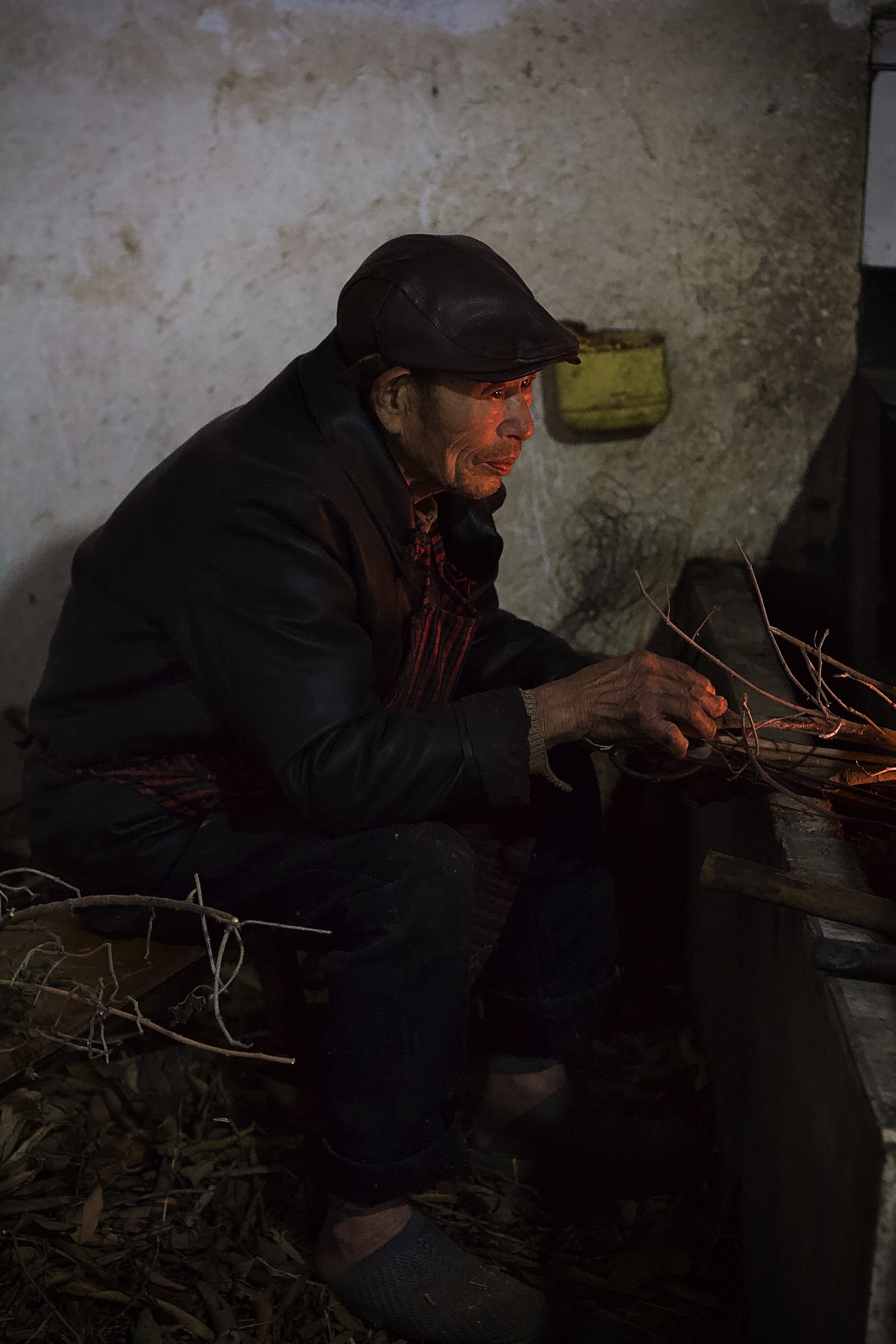 An elderly Chinese man stokes a cooking fire in a traditional Chinese home stone stove.