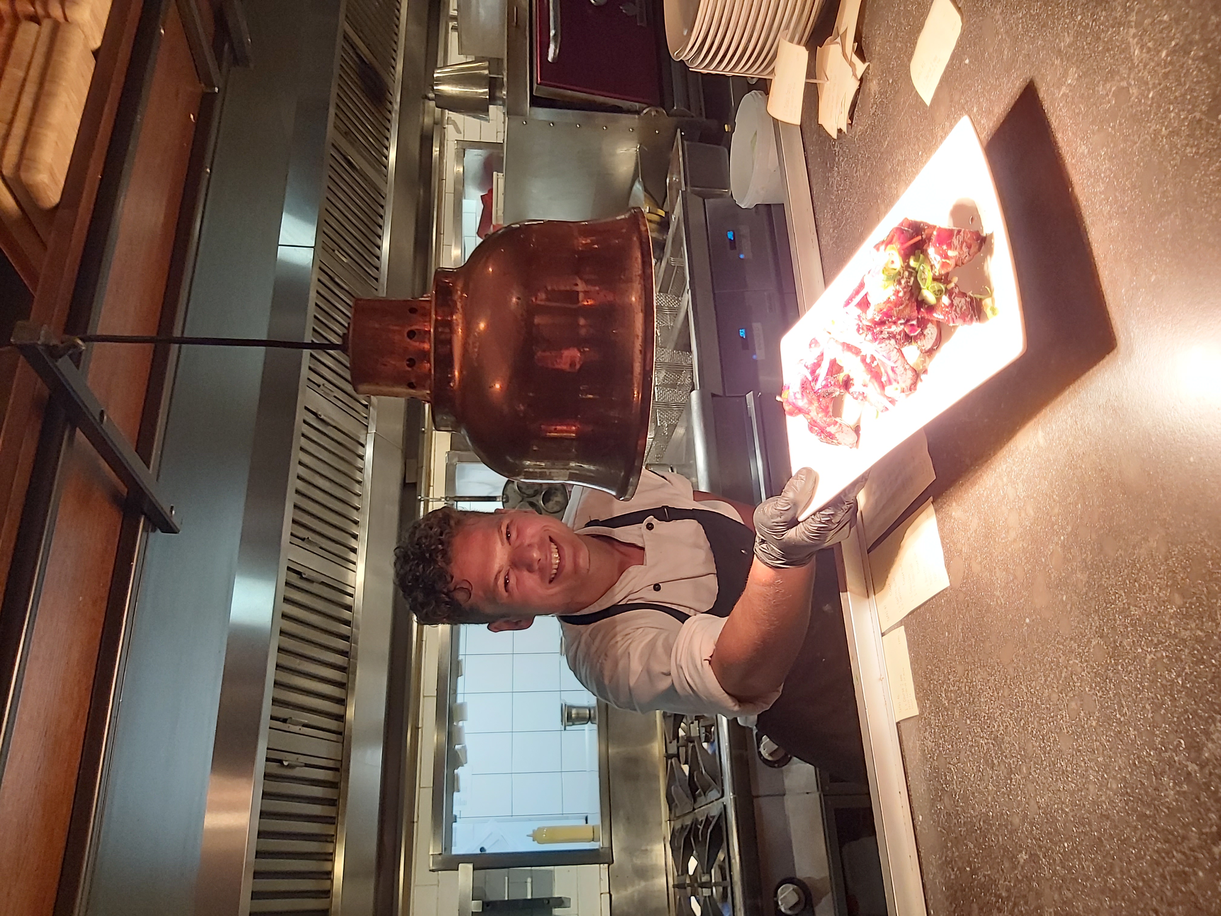 Arnold presenting a dish to front of house staff through the kitchen window at a restaurant in Europe.