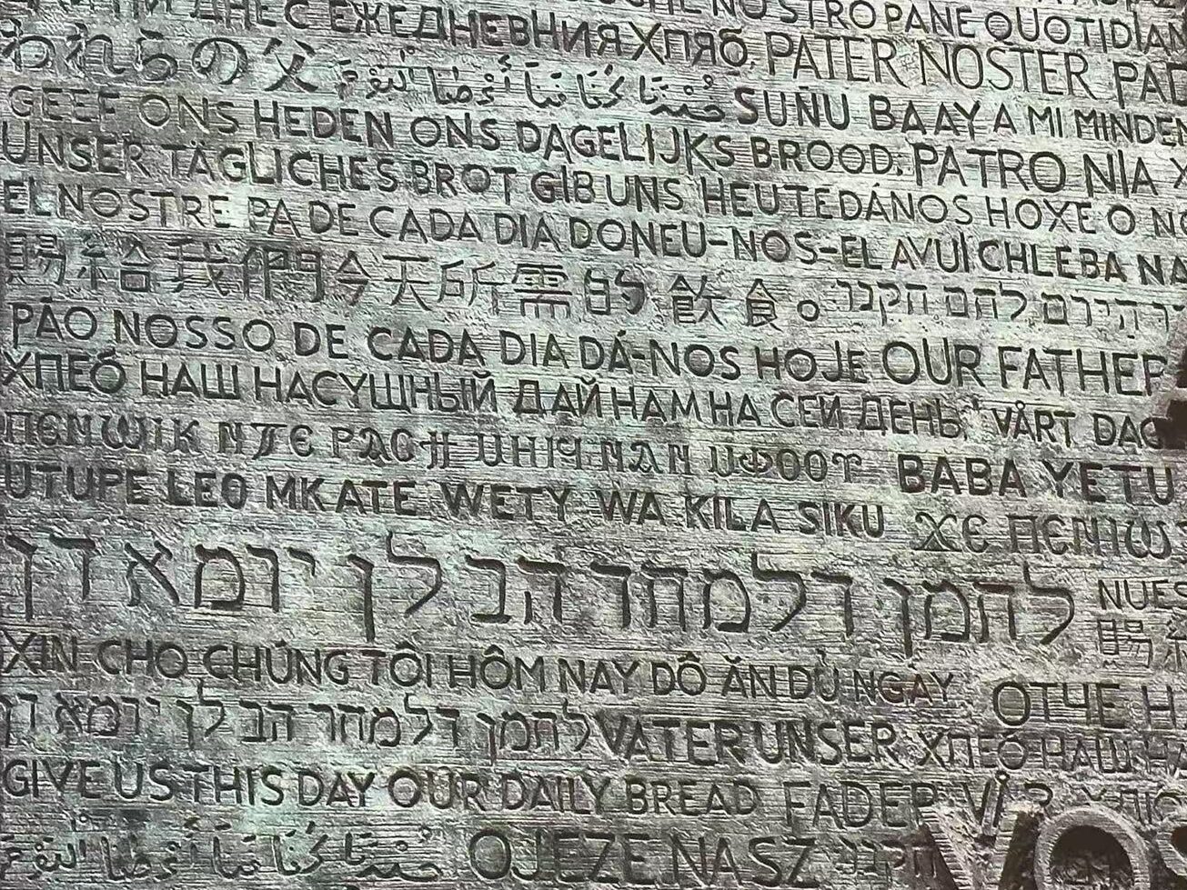 A close up of the multi-cultural wall at the Sagrada Familia in Spain that reads "GIVE US THIS DAY OUR DAILY BREAD" in dozens of languages.