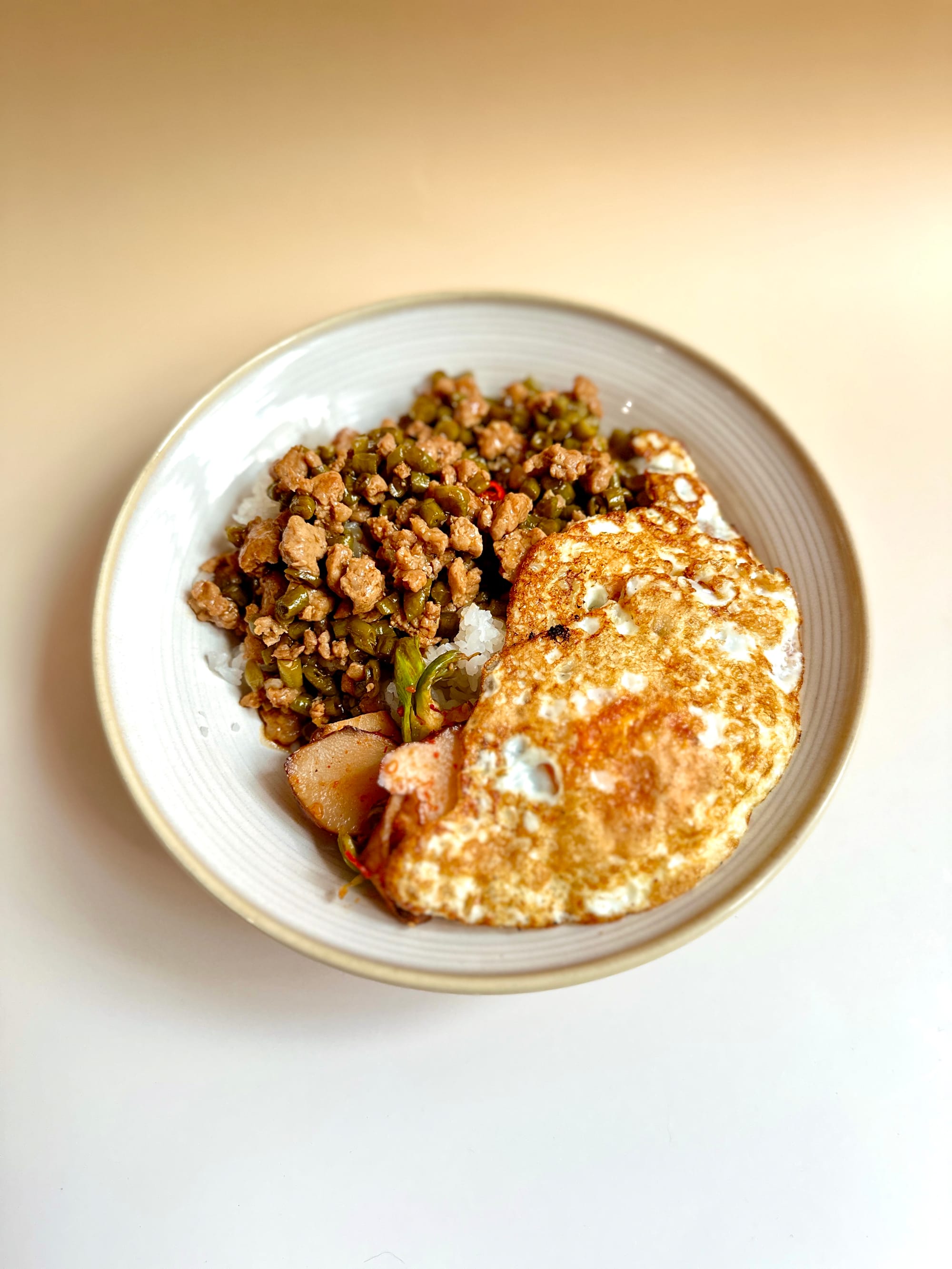 A white bowl with minced pork and pickled long beans stir-fried next to a fried egg.
