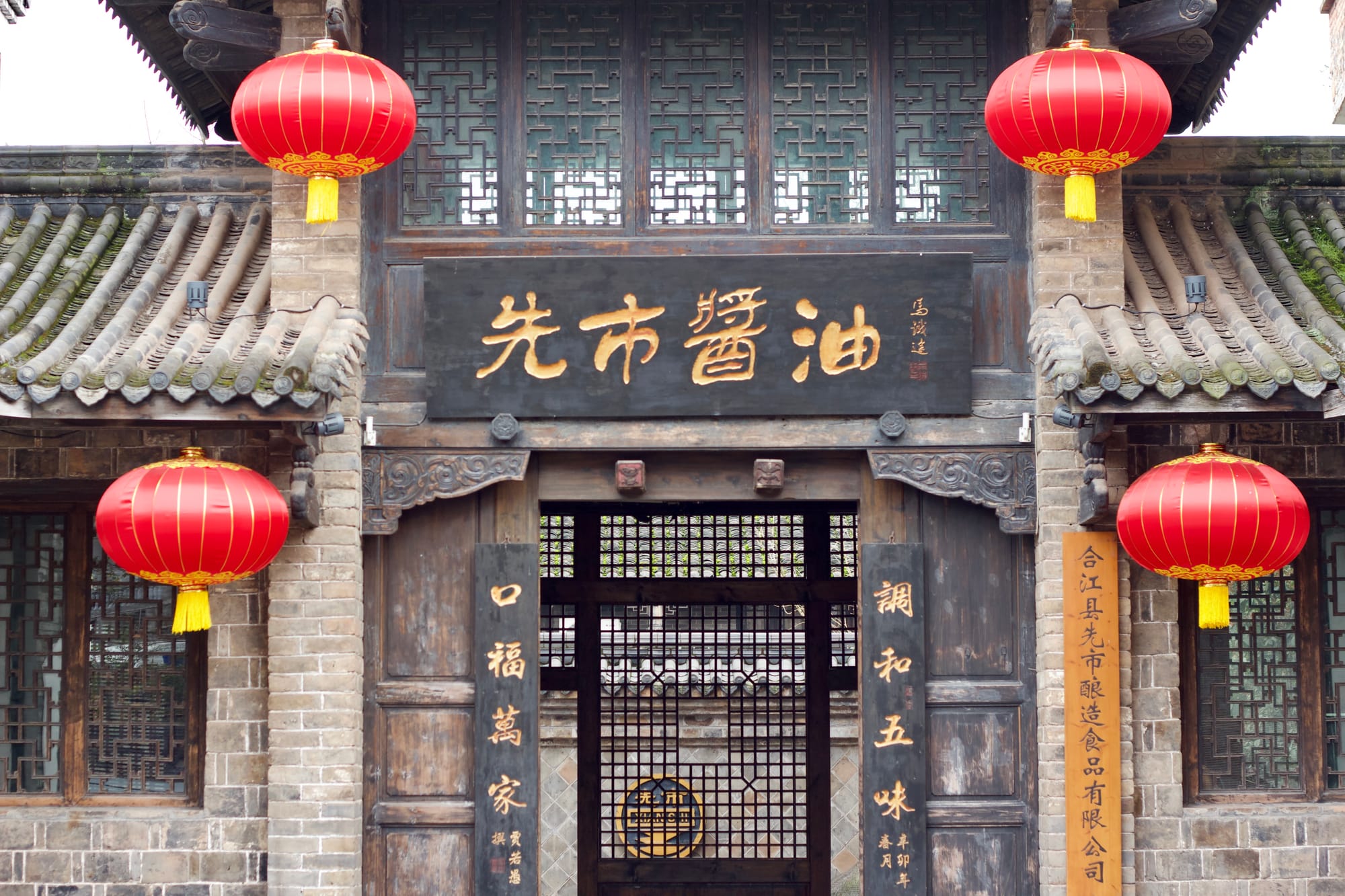 Old Chinese stone and wood architecture. The main wooden gate of a soy sauce factory in Luzhou, flanked by two red lanterns.