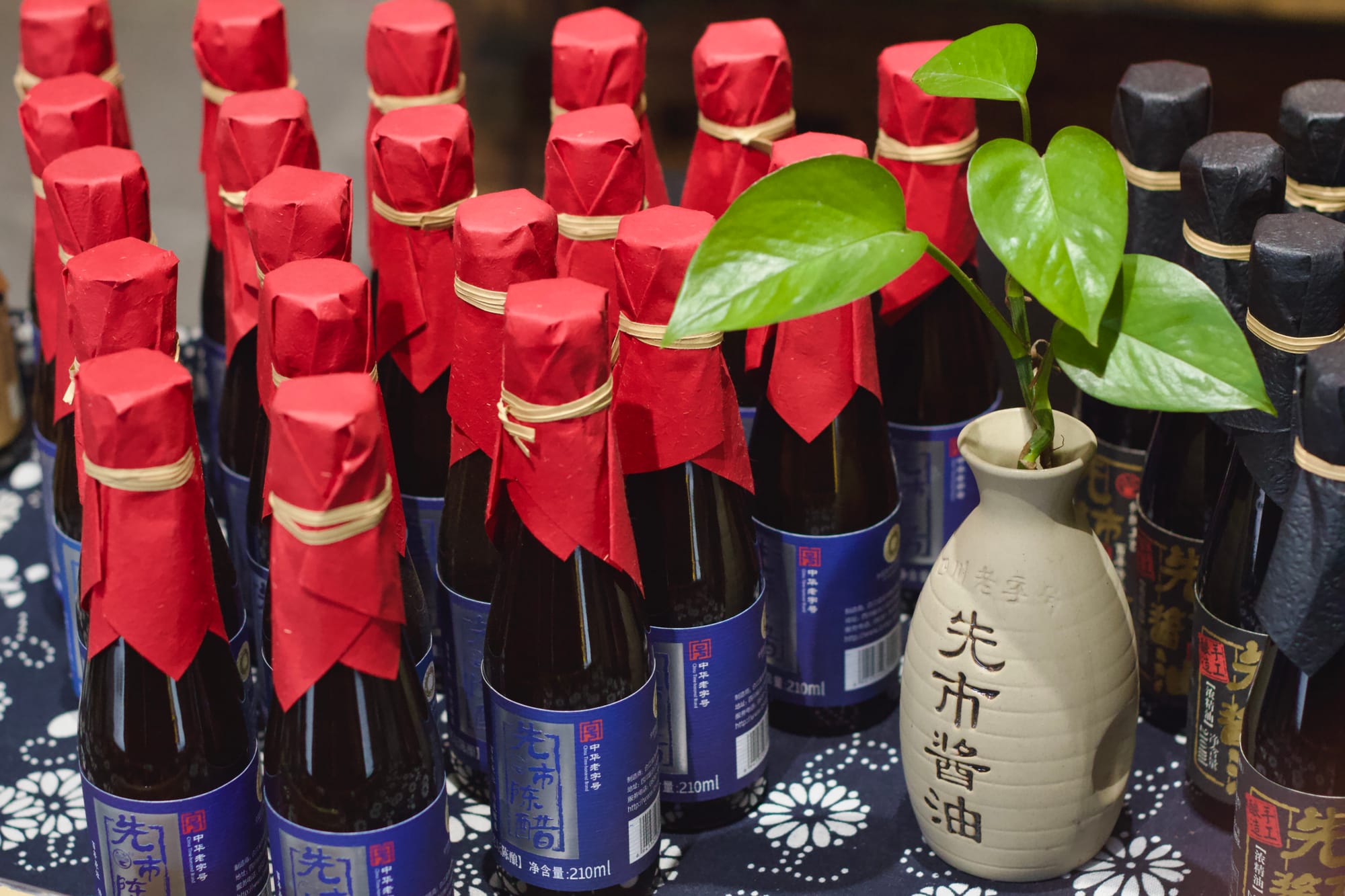 A table with dozens of light and dark soy sauce bottles, wrapped with red and black paper around their tops in a traditional Chinese style.