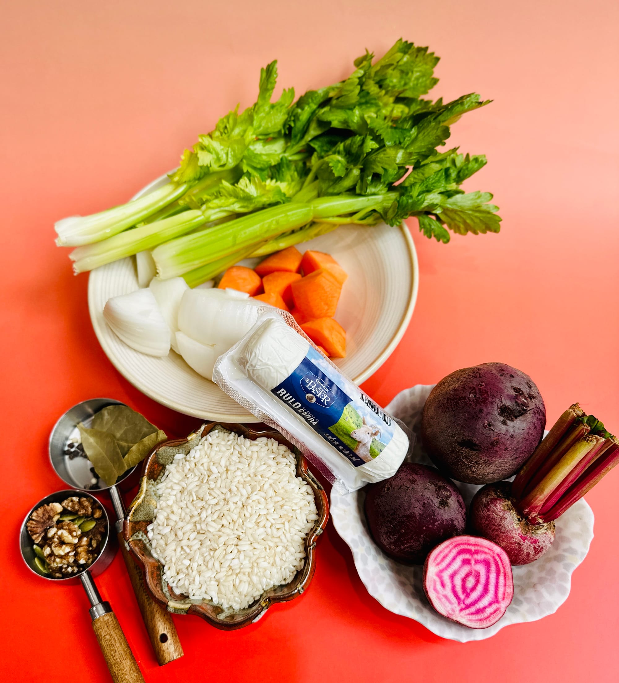 Ingredients for Red Beetroot Risotto - red beets, walnuts, rice, bay leaves, onion, goat cheese, celery, and carrots arranged on a red gradient background.