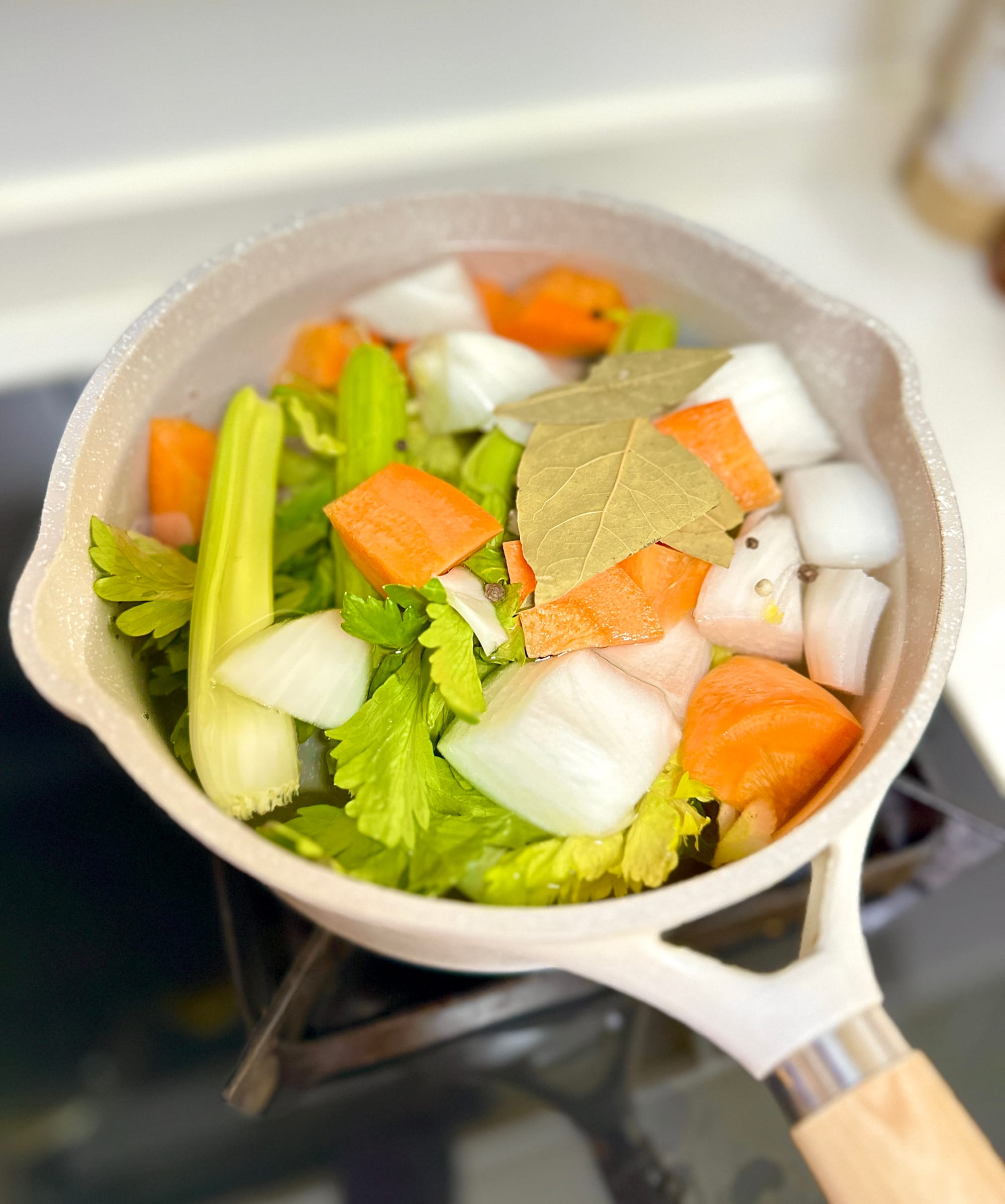A pot filled with the base ingredients for the vegetable broth - white onions, carrots, celery, bay leaves, and spices.