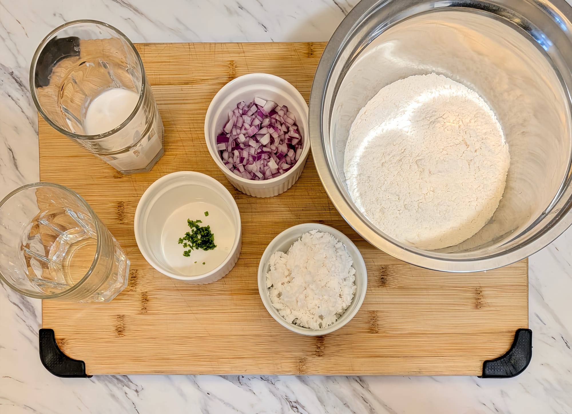 On a marble backdrop, a bamboo cutting board sits with the dishes of measured out ingredients for Pol Roti