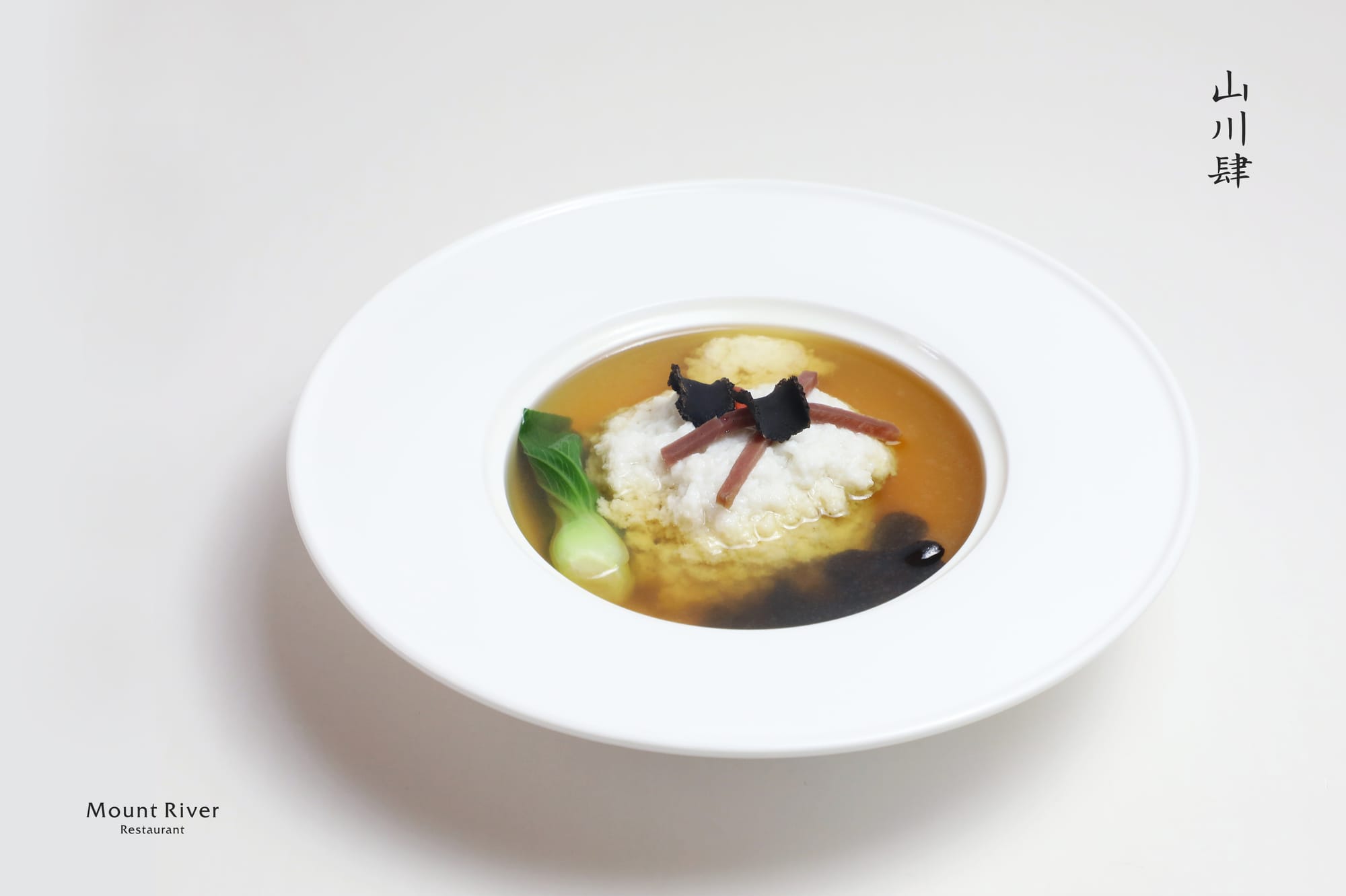 A white bowl with a wide rim, filled with golden chicken broth, a single bok choy, 3 black fungi, and a minced chicken cloud to simulate the texture of tofu, presented on an off-white background.
