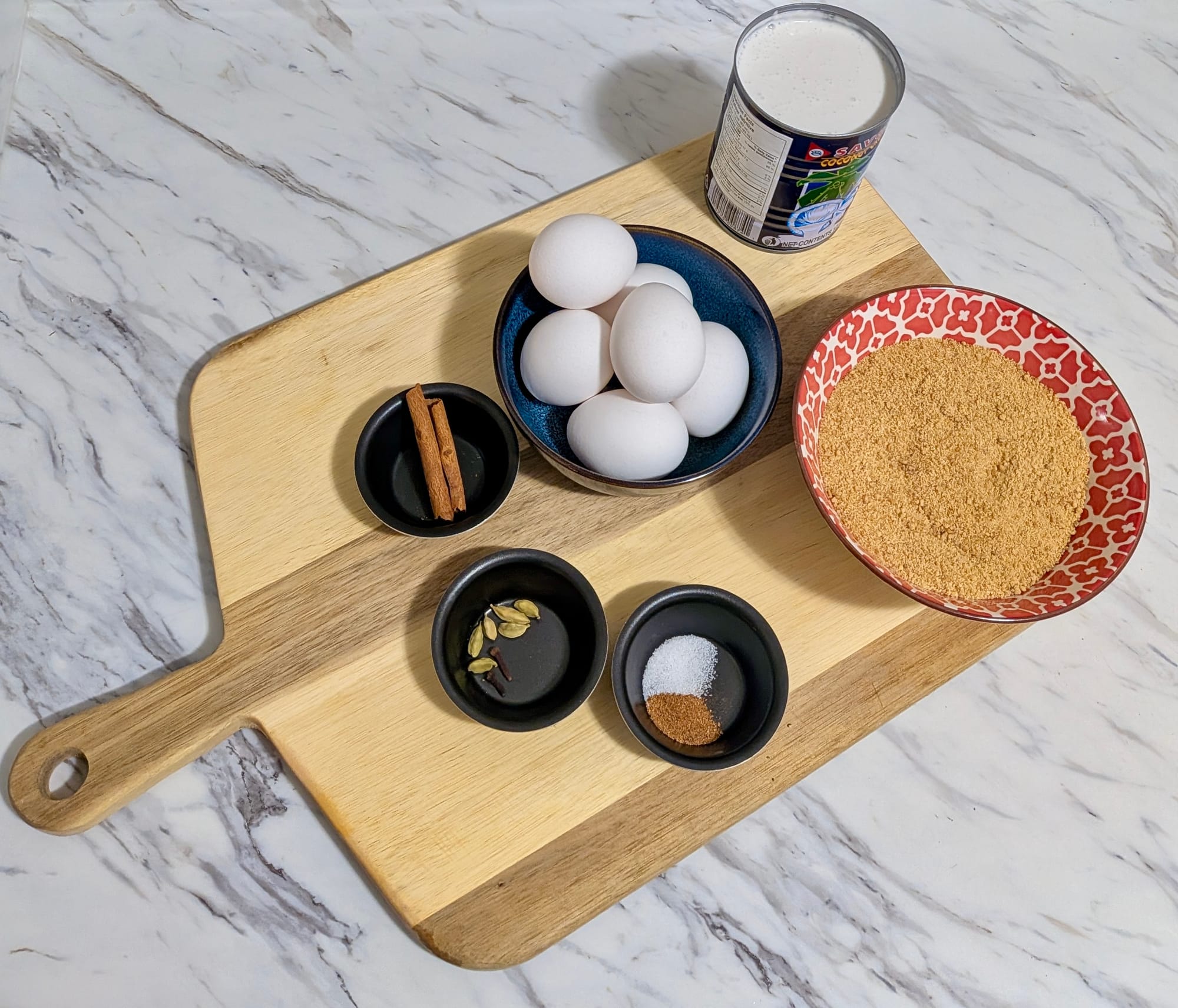 Small dishes and bowls filled with the ingredients used for Watalappam, on a serving board.