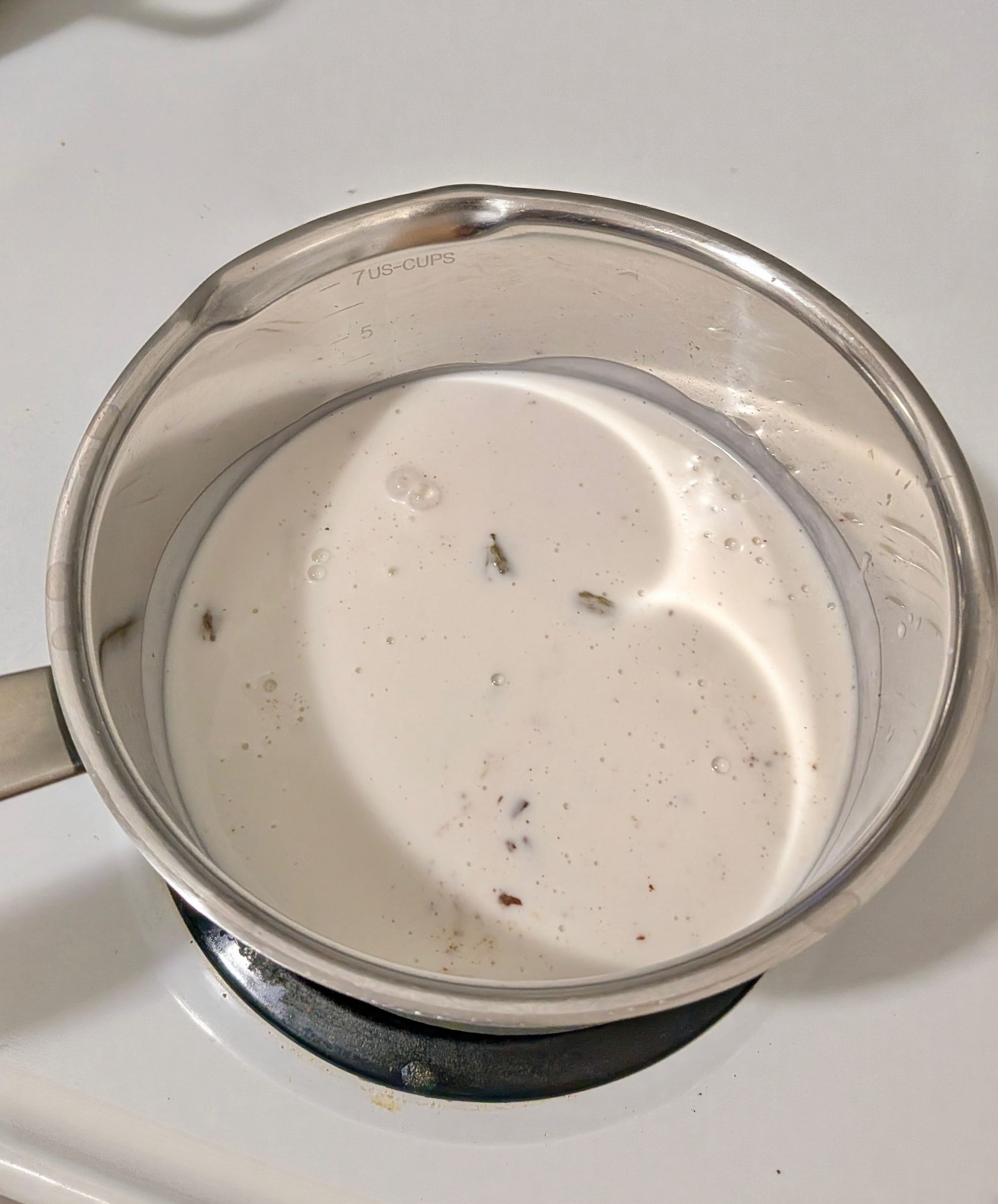 Coconut cream and spices mixed together in a pot on a white stove.