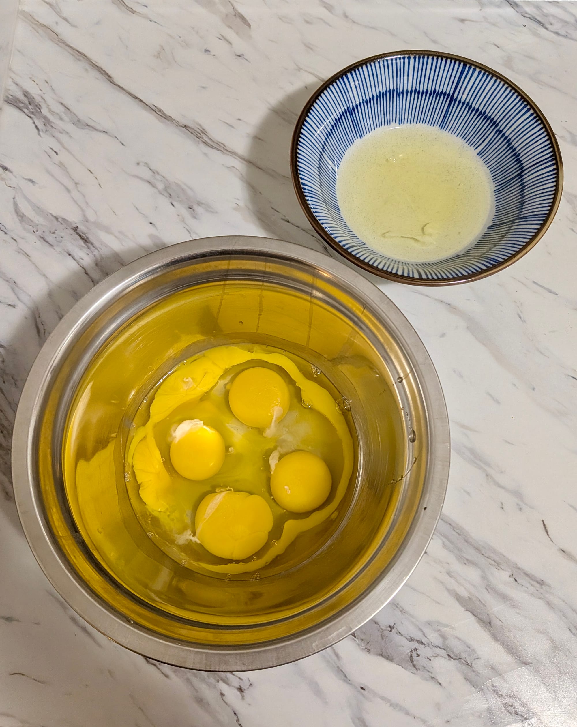 Two bowls side-by-side, one contains 2 egg whites and the other 4 whole eggs plus two egg yolks.