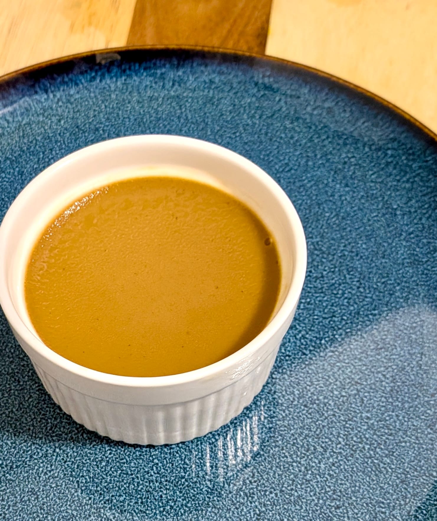 A blue plate with a white ramekin on top filled with Watalappam - a light brown Crème Brûlée-like dessert.