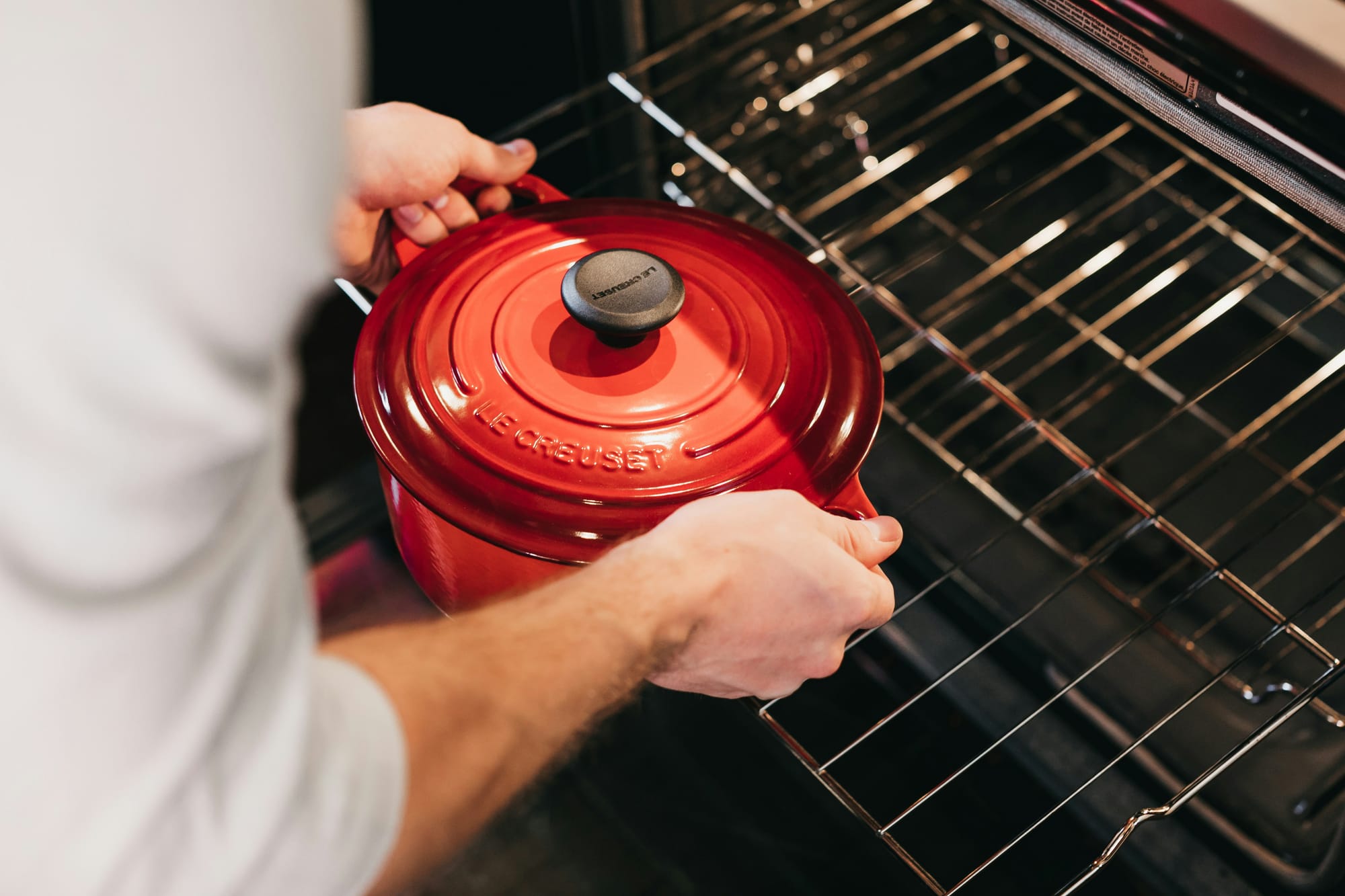 A chef placing a red Le Creuset crockpot into an oven