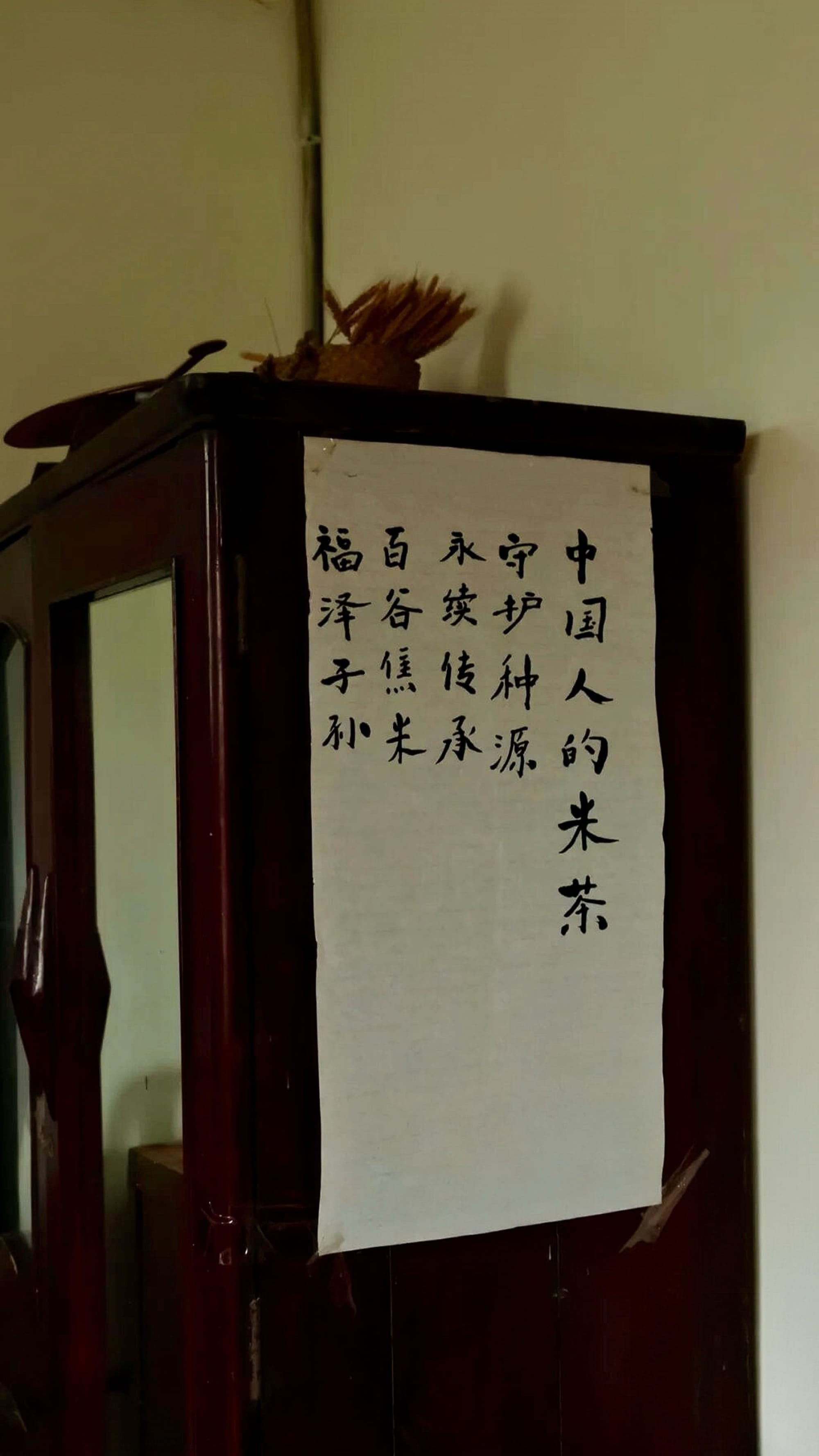On the back of a dark wooden door, a white paper sign with black hand-written calligraphy features Chinese characters.