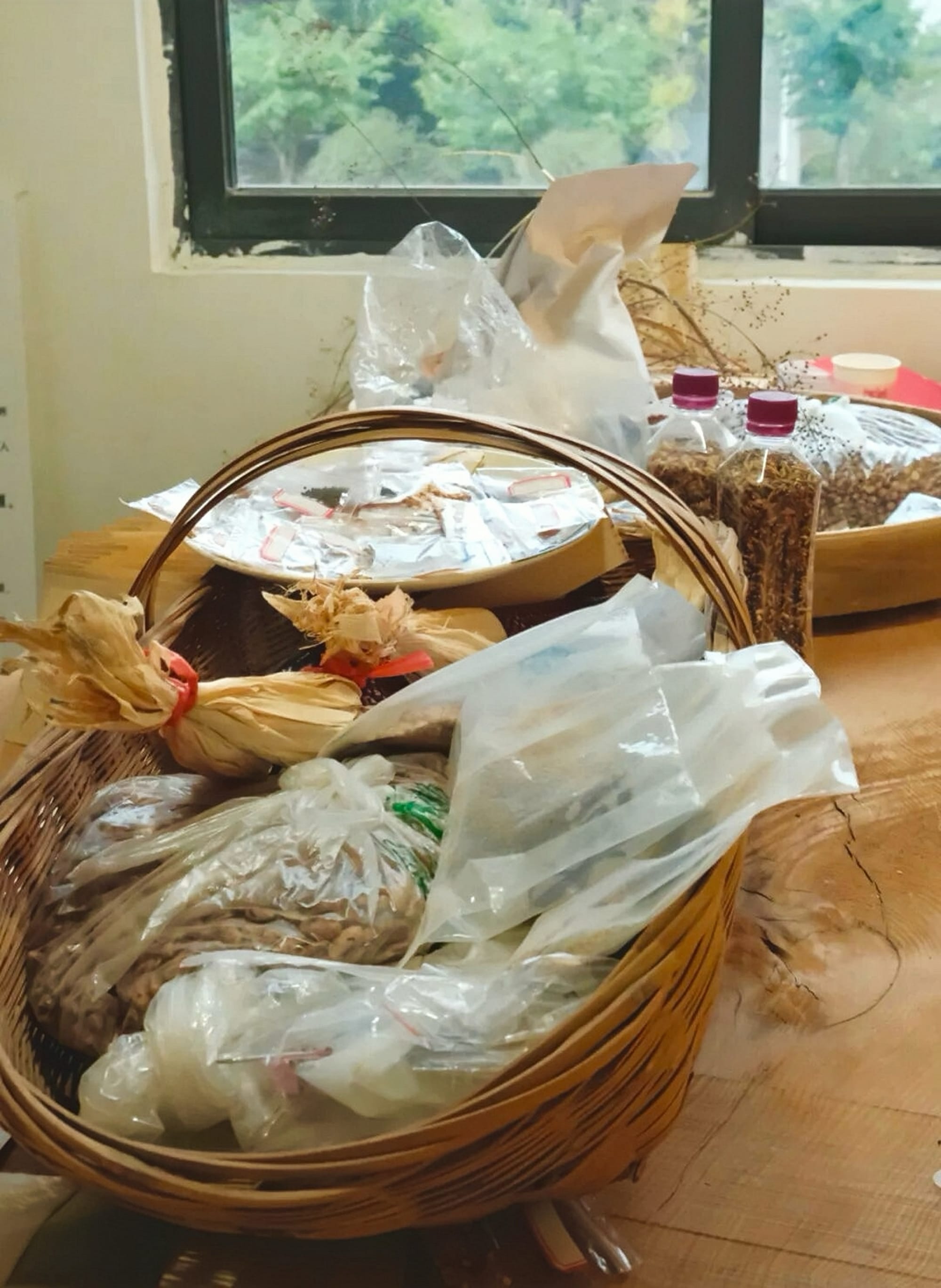 A medium sized bamboo basket is filled with bags of seeds for different species of plant.