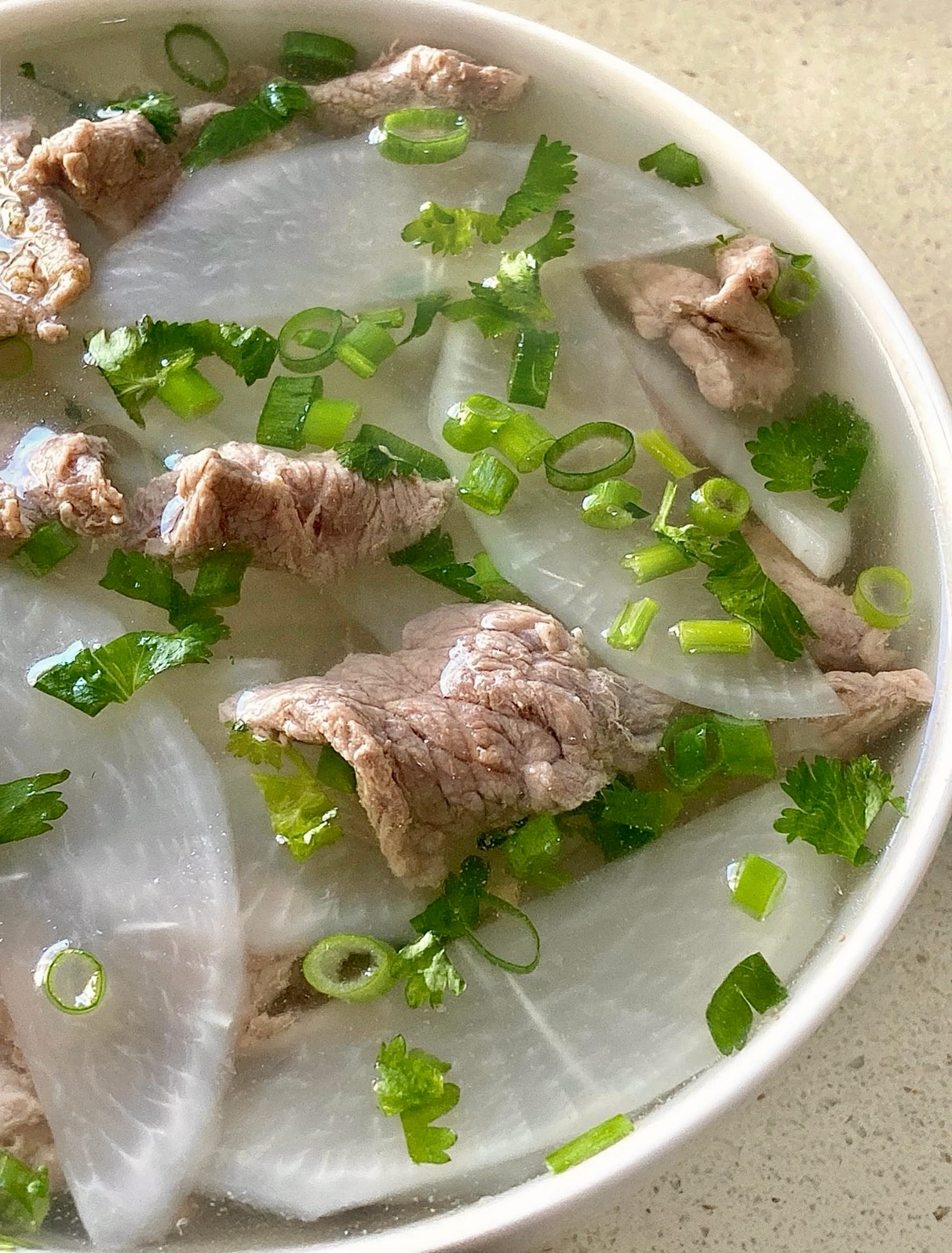 A bowl of thinly sliced radish and beef with onion and coriander. 
