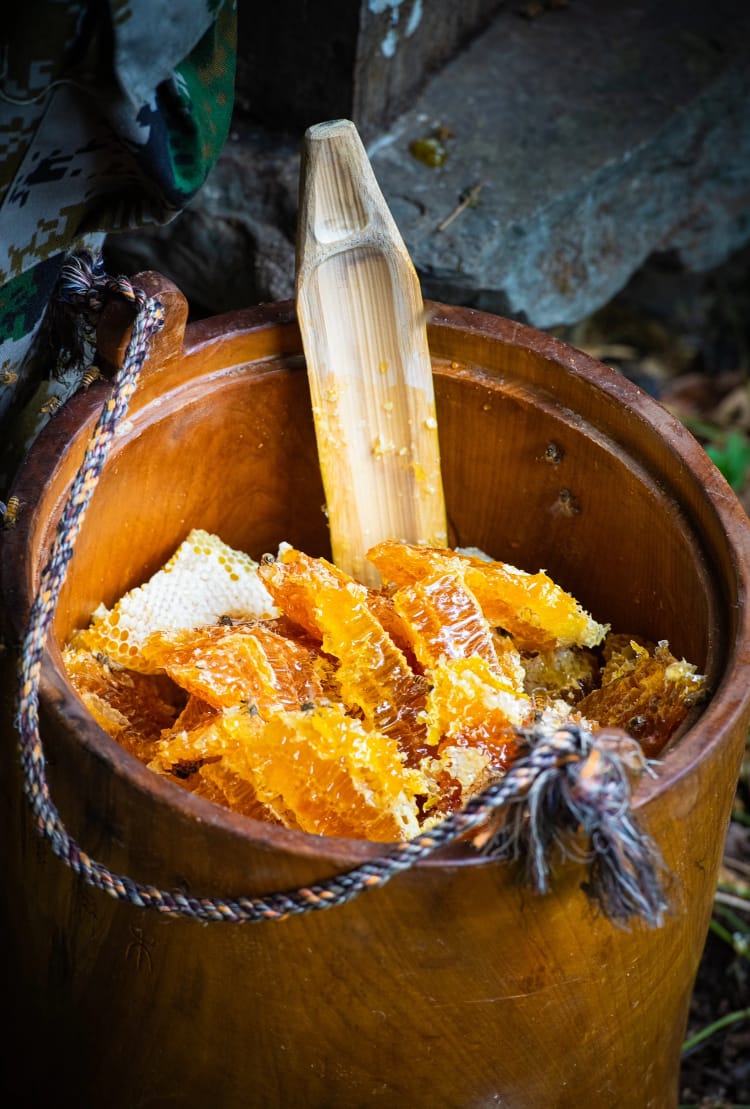 A wooden bucket with rich golden honeycombs and a piece of bamboo sticking out used to break and crush them to release the honey.