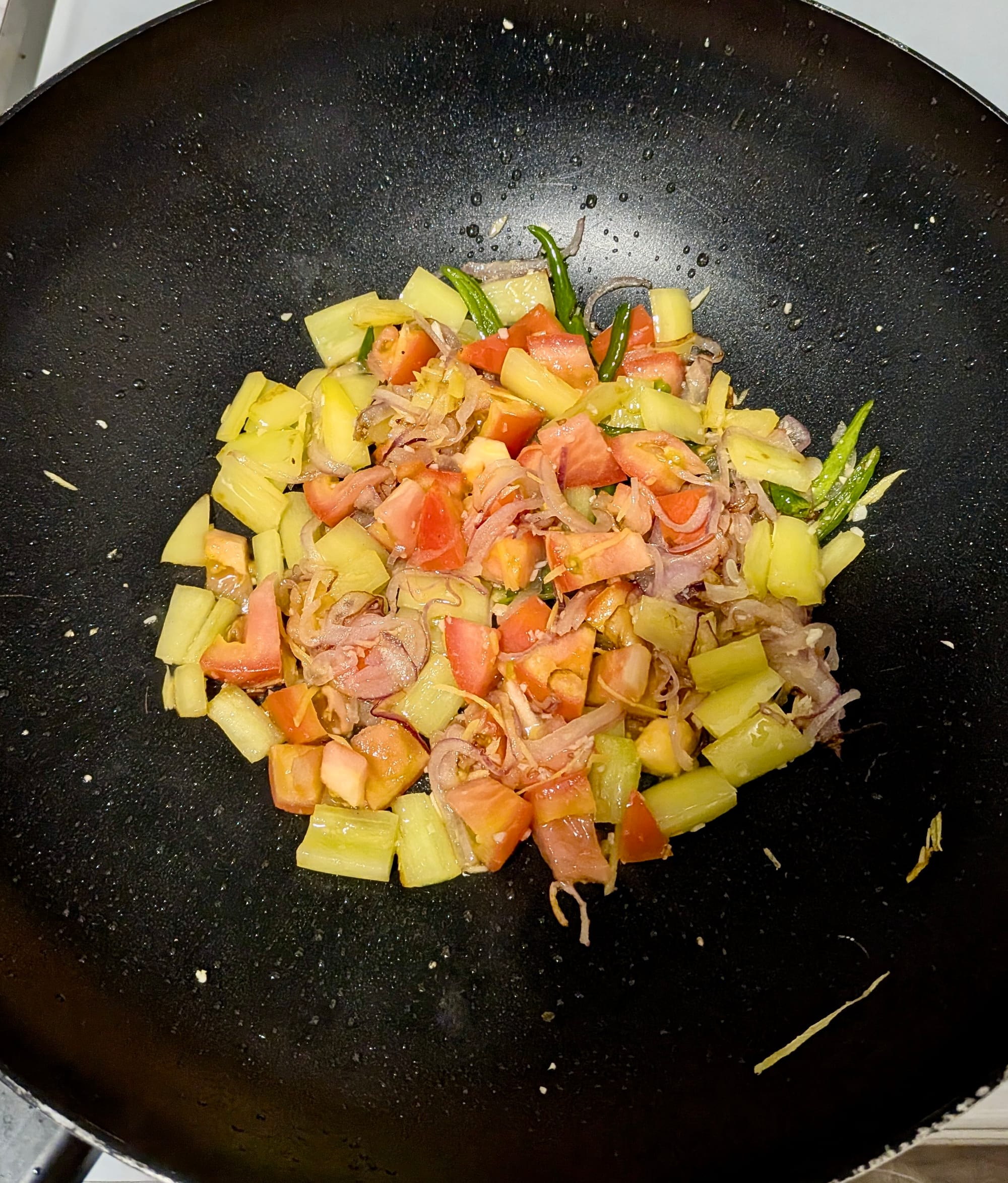 A wok filled with diced yellow pepper, tomato, coconut oil, red onions, and green chili.