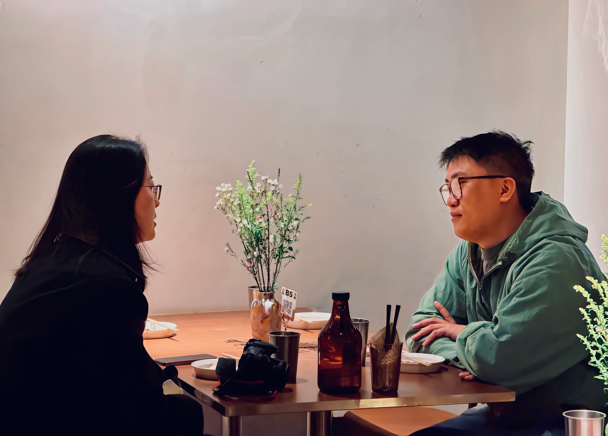 Chloe Wang sits at a table, interviewing Wei Yuan about his restaurant.