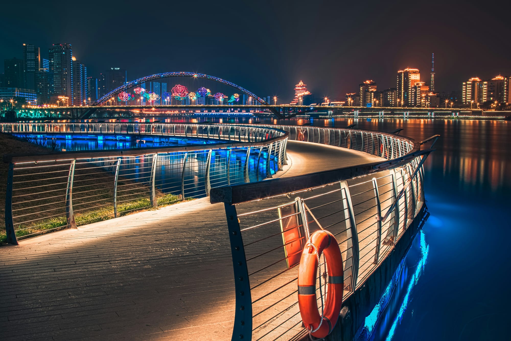 Mianyang, boardwalk in Sichuan Province, China, lit up at night with a rainbow city in the background.