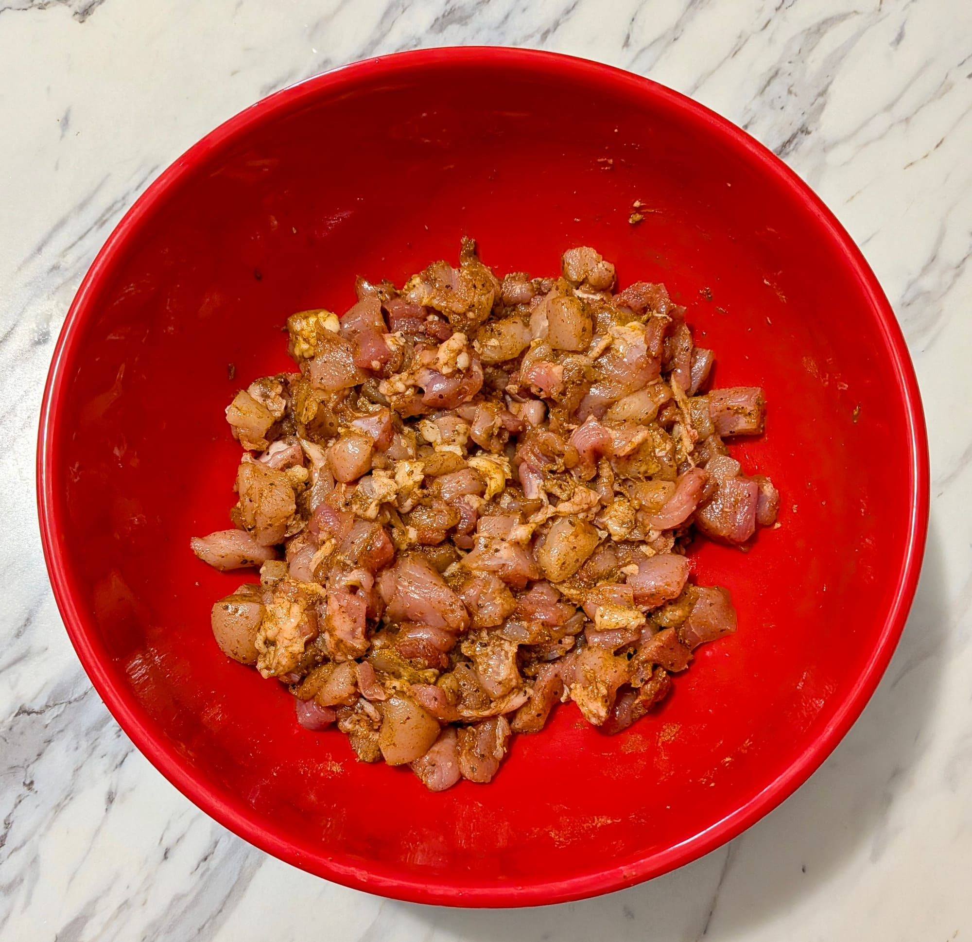 Minced chicken mixed with spices in a red bowl.