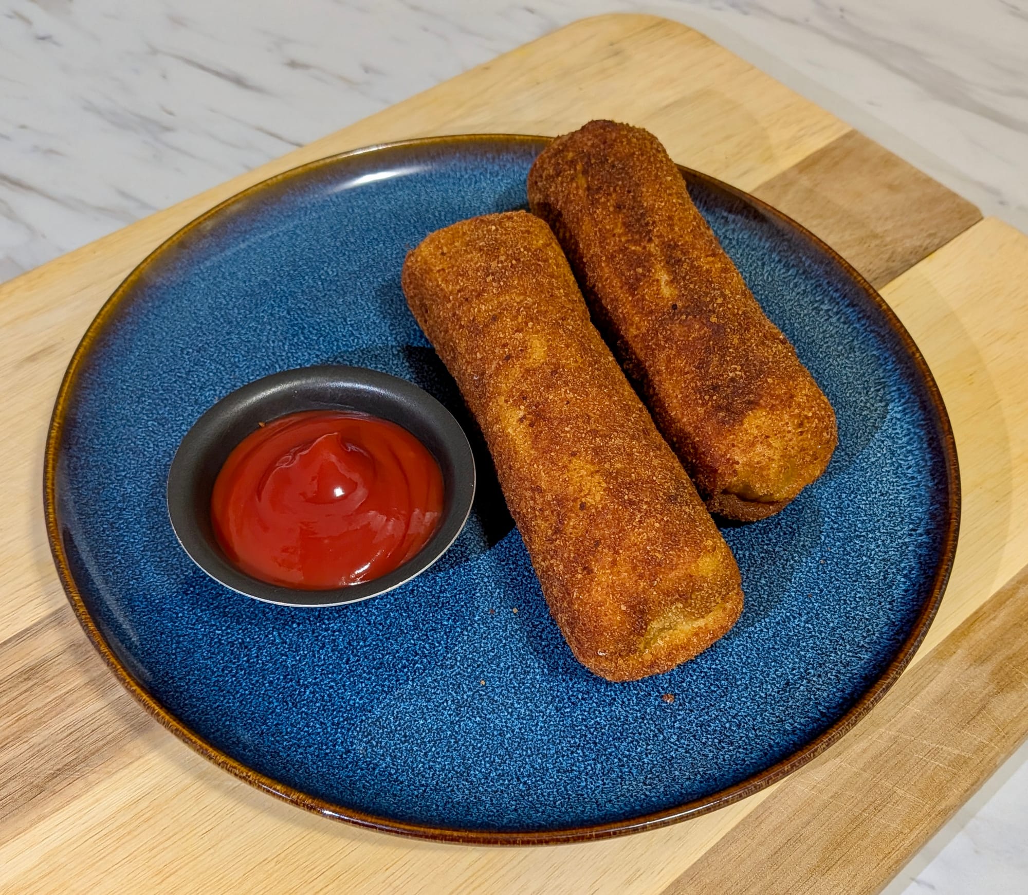 Two fried chicken rolls, golden brown, plated next to a ketchup dipping cup.