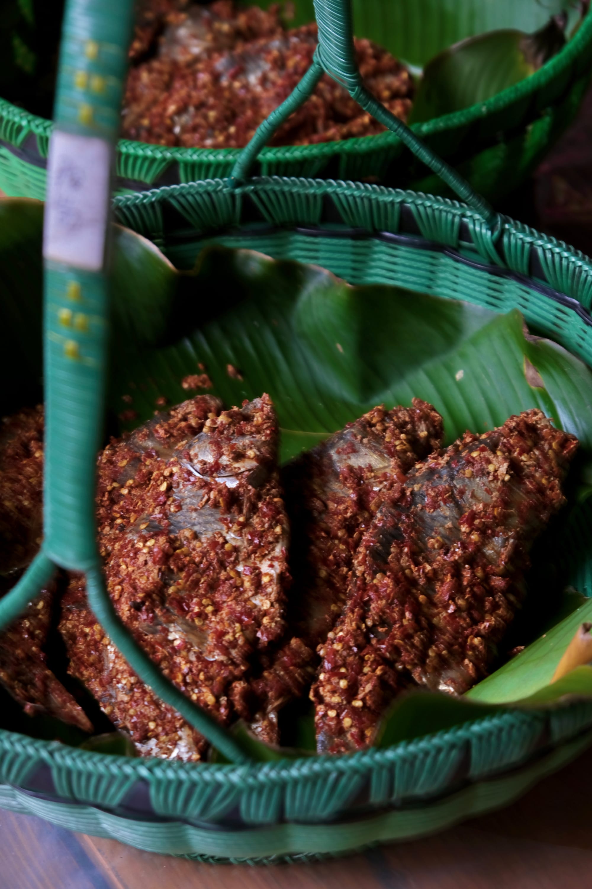 A plastic basket with large green leaves holds chili-coated fermented fish.