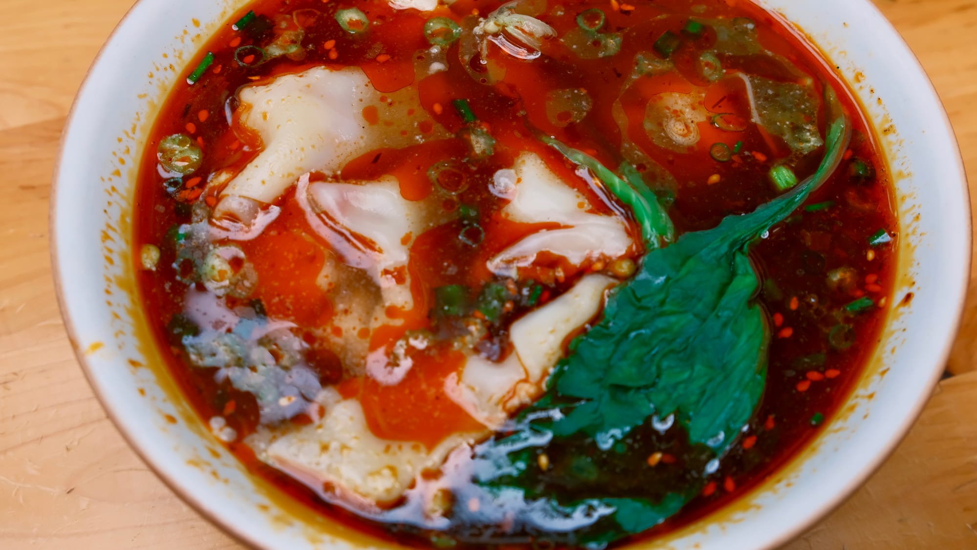 Doubanjiang wontons in a bowl with chili oil and coriander.