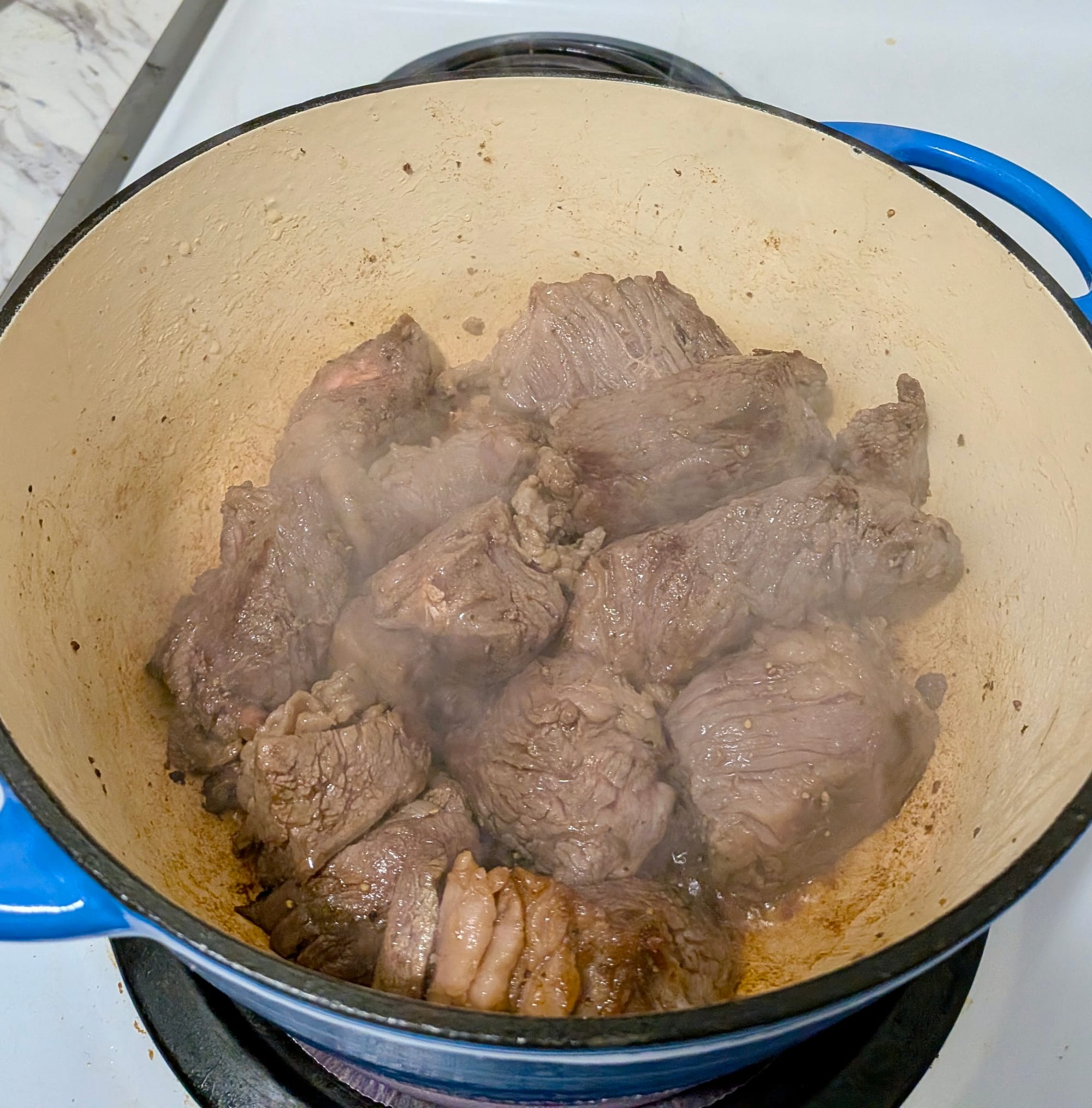Chunked beef cubes sweating in a pot on the stove.