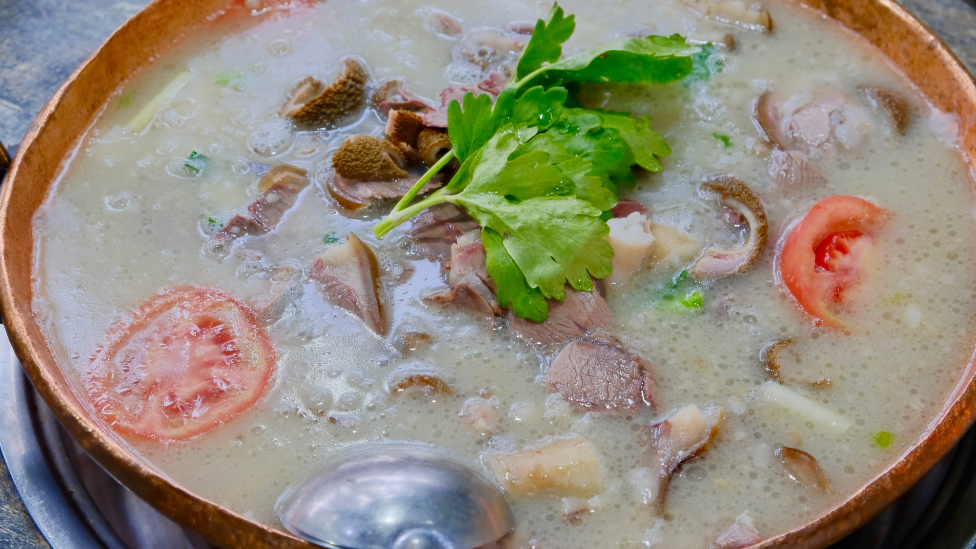 Goat soup, a white broth filled with chunks of goat meat, tomatoes, and parsley on top.