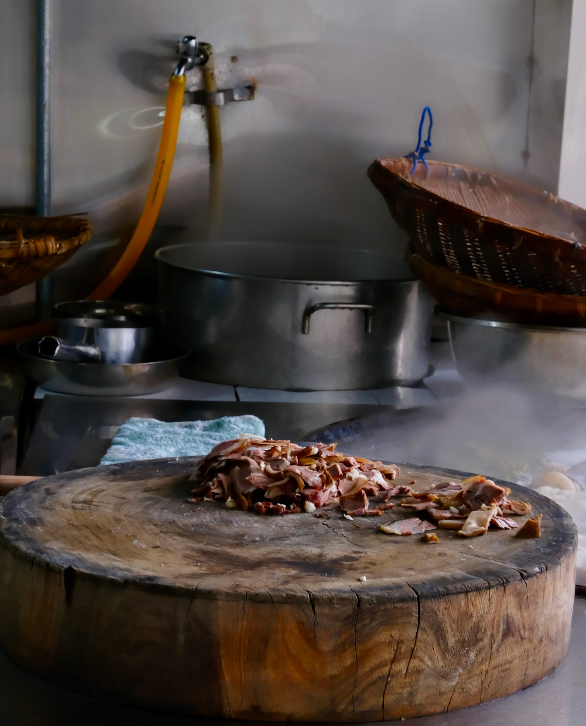 A sliced log serves as a cutting board in a kitchen, atop it sits shaved goat meat.