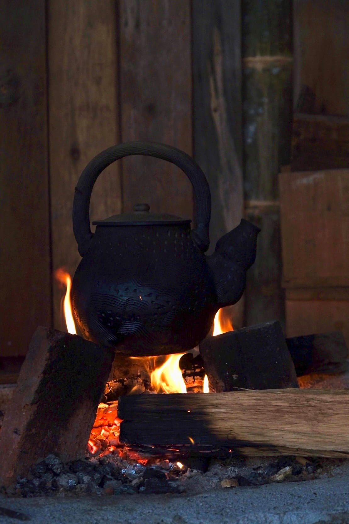 A wood fire heats a blackened kettle for tea.
