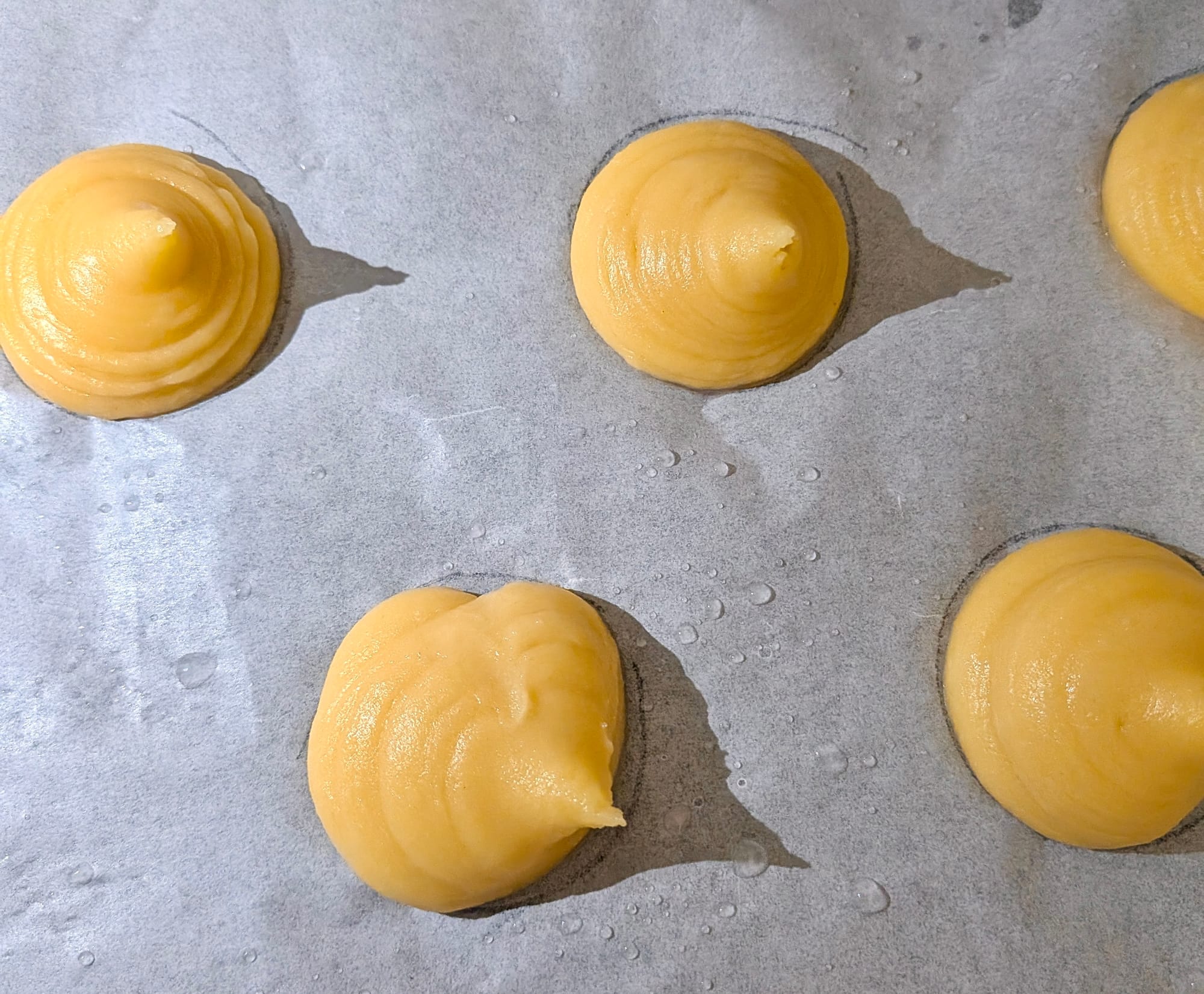 Parchment paper with 5 circular piped cones of yellow-ish choux.