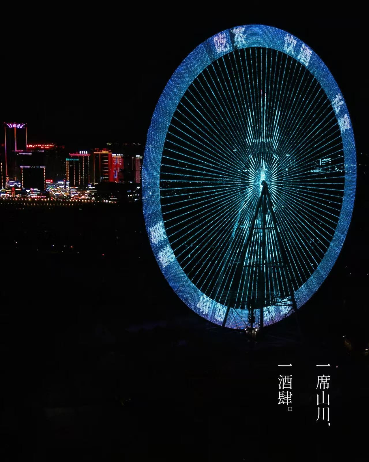 The Luzhou Ferris wheel lit up at night time with blue lights along the rim and spokes, with white Chinese characters along the rim, the black city in the background speckled with other buildings bedazzled in neon lights.