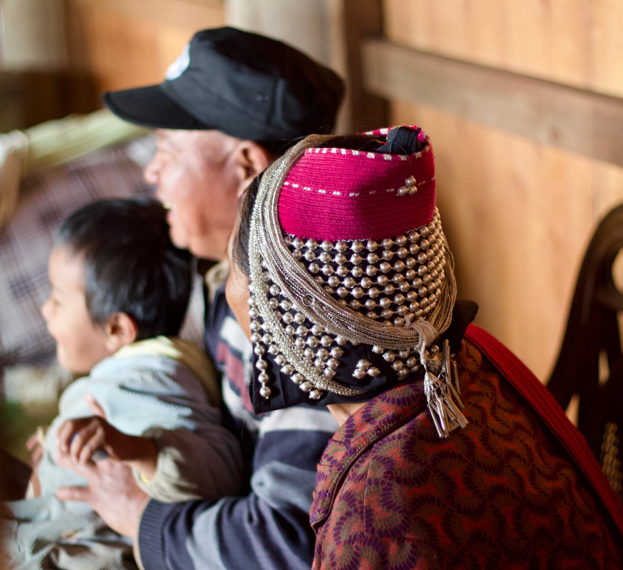 A traditional Wa family sits at a wedding, the grandmother close up in her steel-beaded and chained hat.