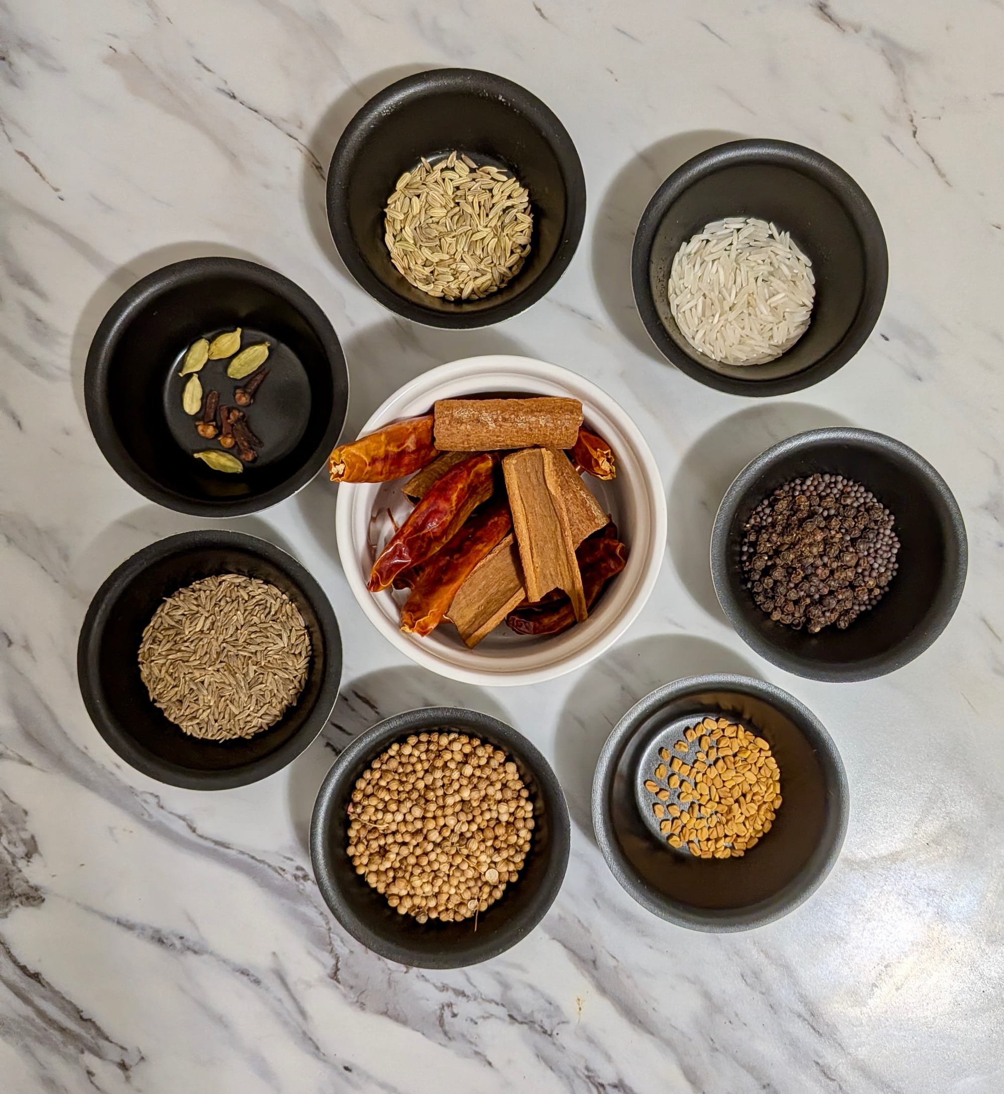 Spices for homemade curry powder portioned in little dishes on a white marble counter top.