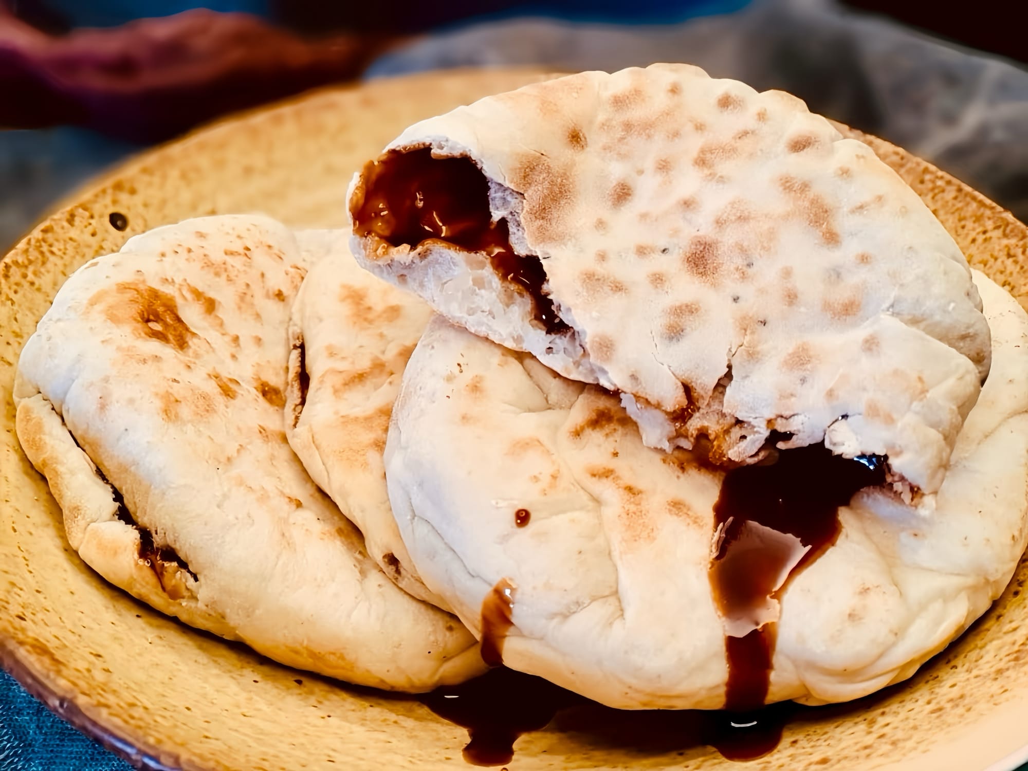 Fried bread pockets filled with oozing brown sugar syrup. One is broken and leaks out dark brown liquid sugar.