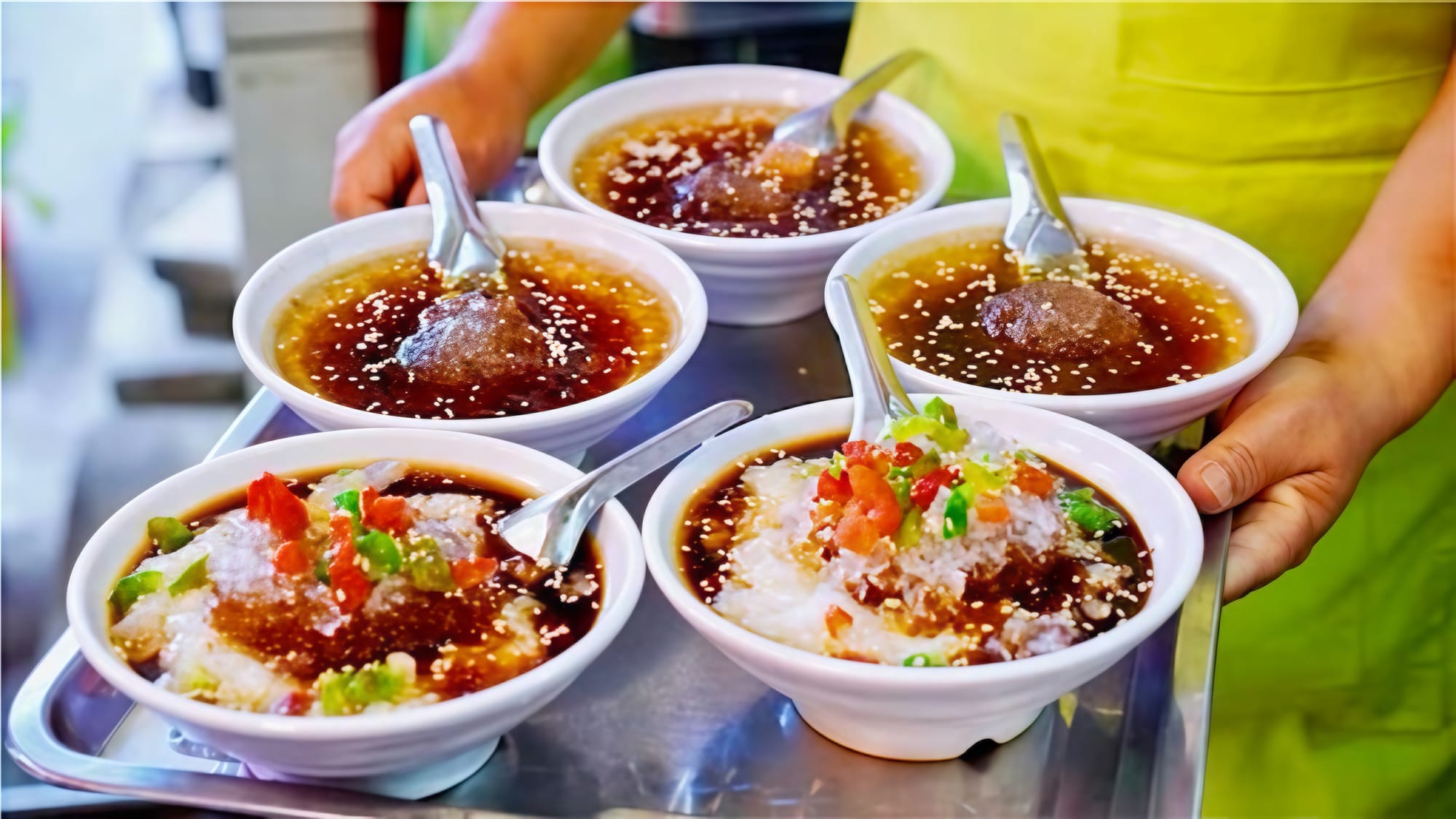 A server holding a tray with five bowls of a sweet, cold fermented rice dish with brown sugar.