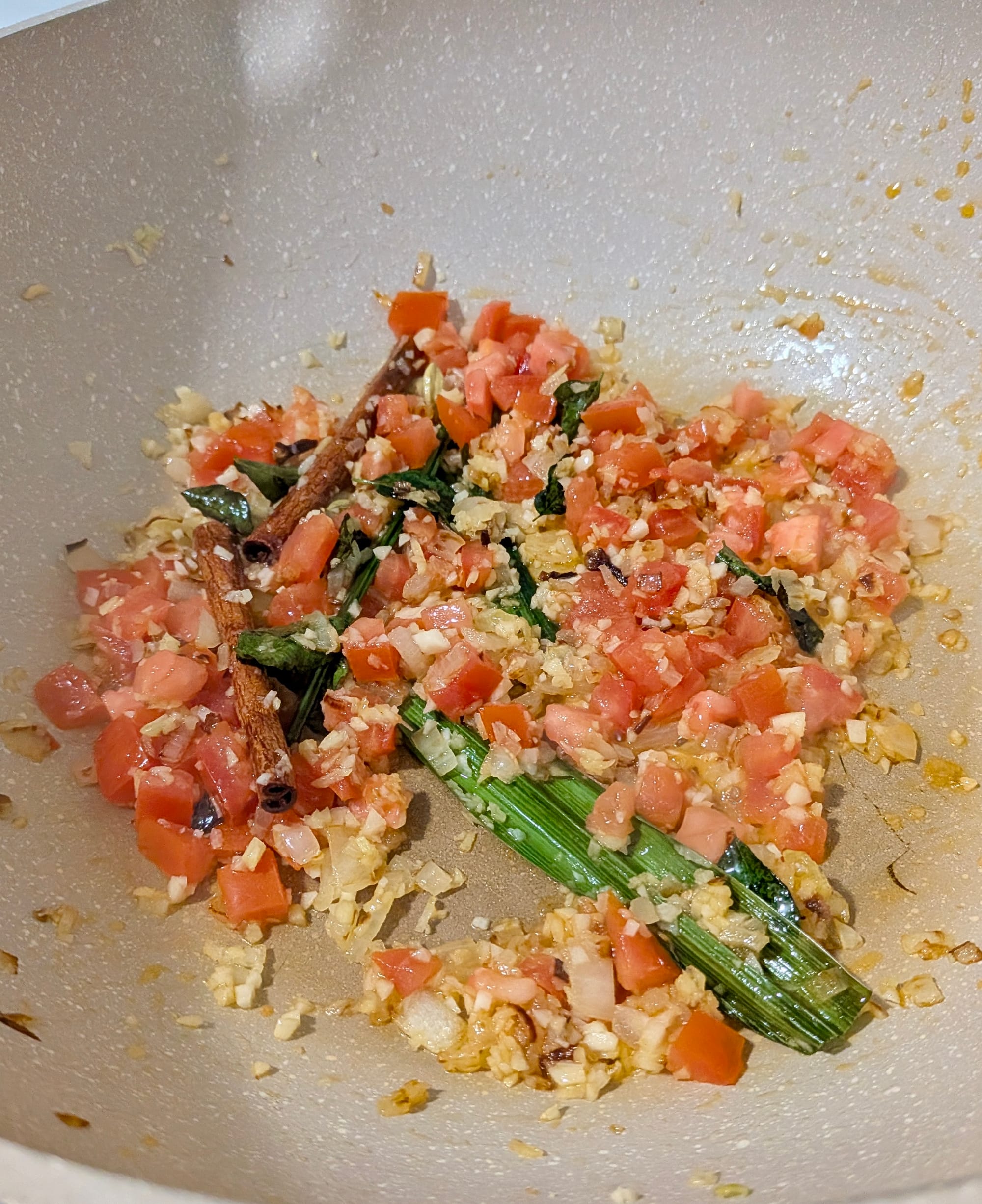 Sweating onions, lemon grass, cinnamon, and diced tomato in a pan.