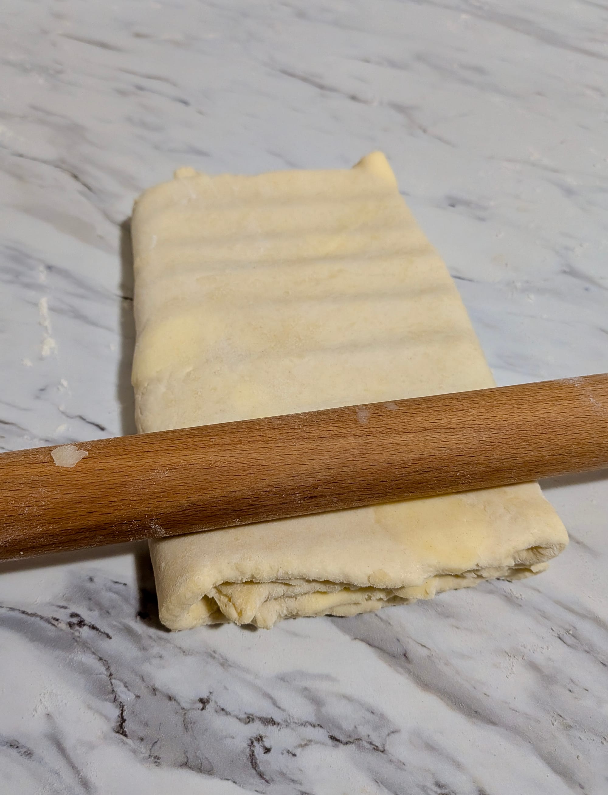 Dough being rolled using a book-fold technique-where the sheets fold over themselves-with a wooden rolling pin.