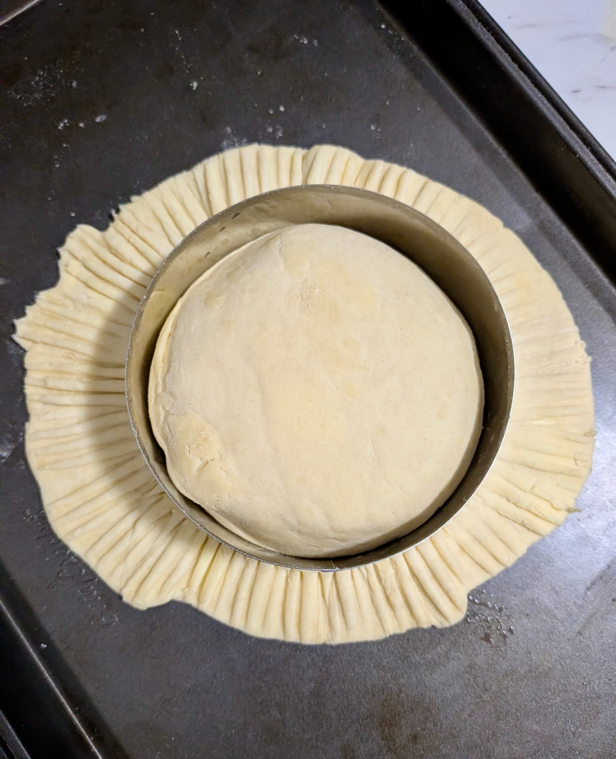 The aerial view of a pithivier being capped - the raw dough placed overtop the filling like a drape then crimped with a ring mold.