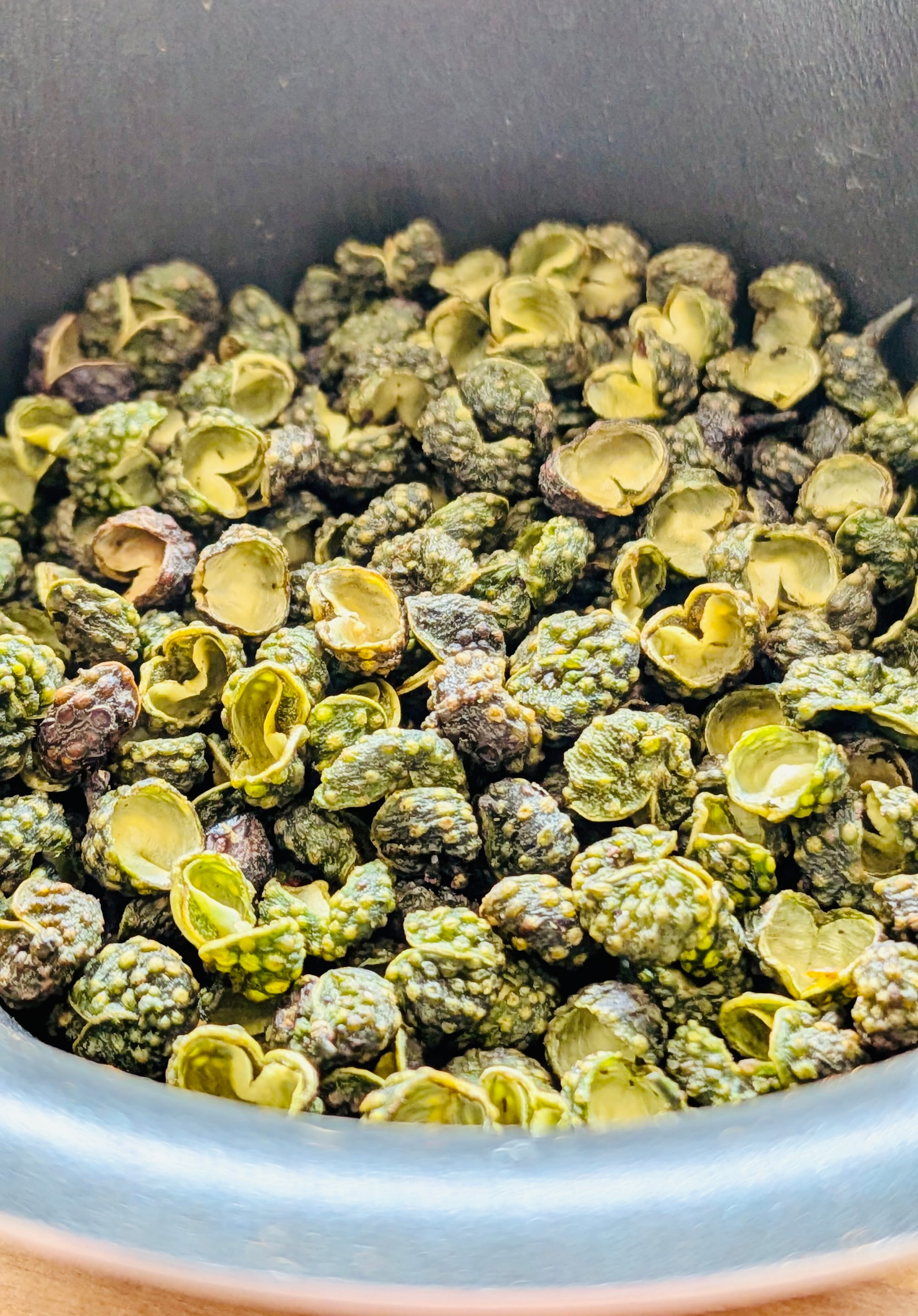 Green Sichuan peppercorns close up - bumpy green pods about 2mm in diameter in a cup.