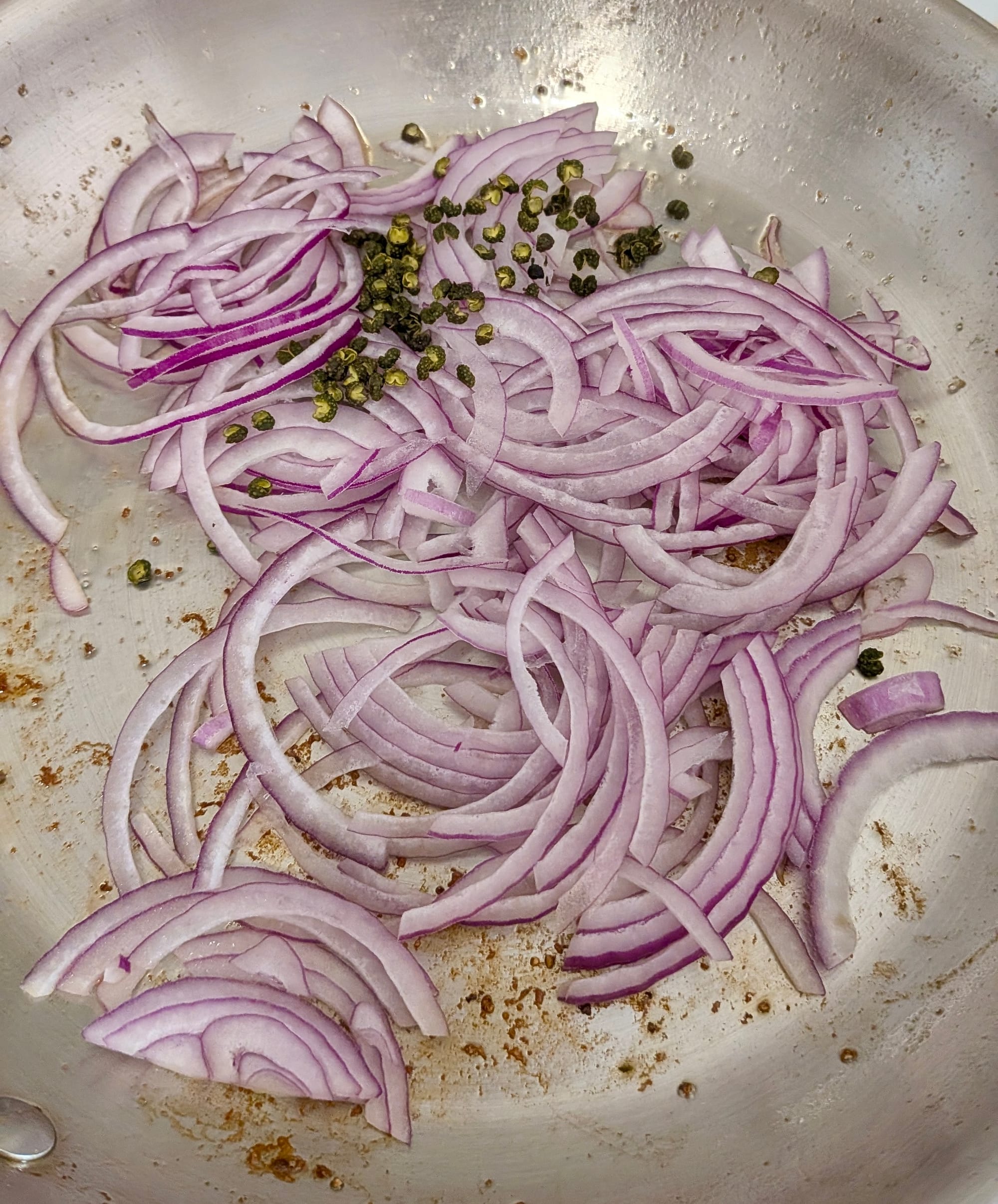 Diced red onions sweating in a stainless steel pan.