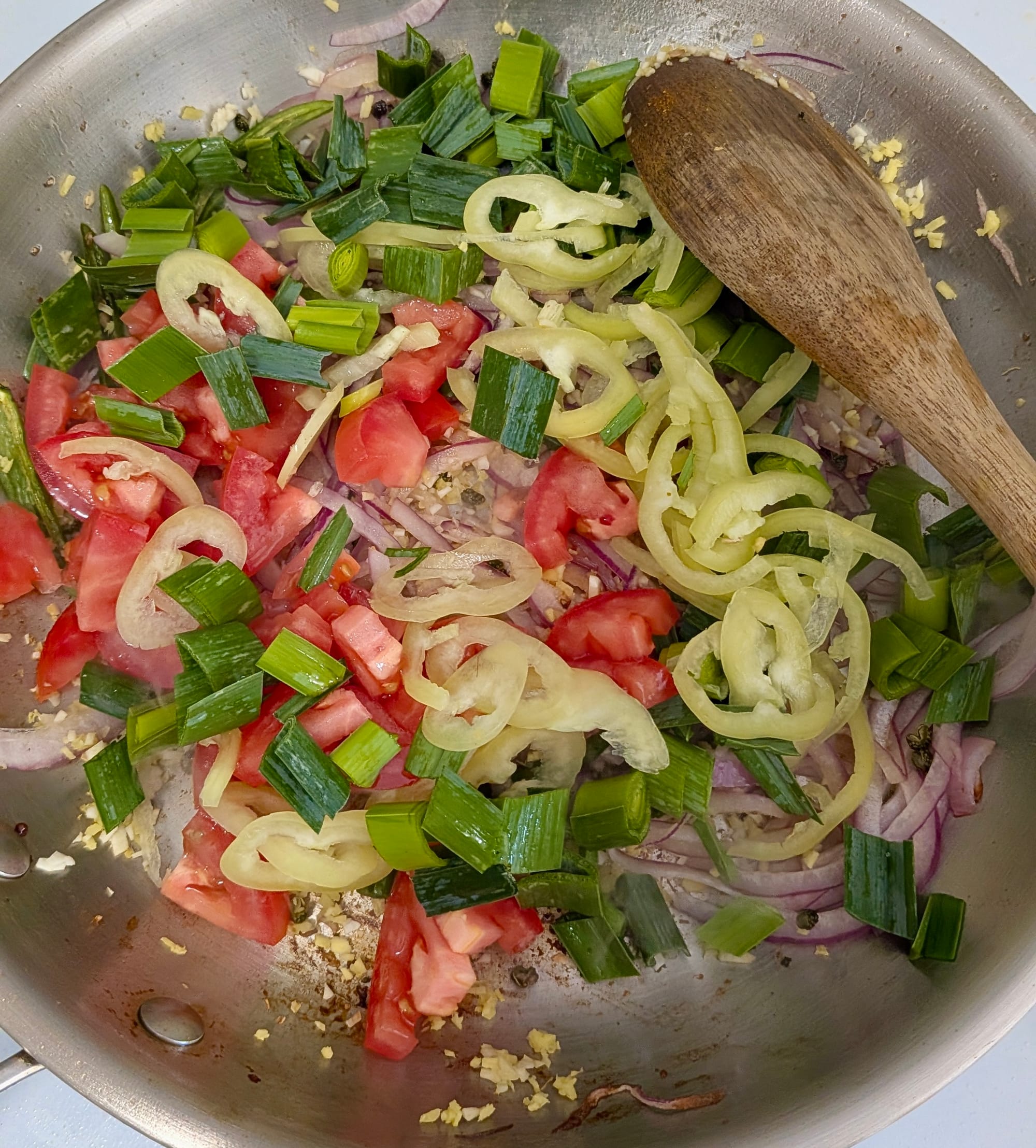 Chopped tomatoes, green onions, red onions, jalepeno peppers sweating in a stainless steel pan.