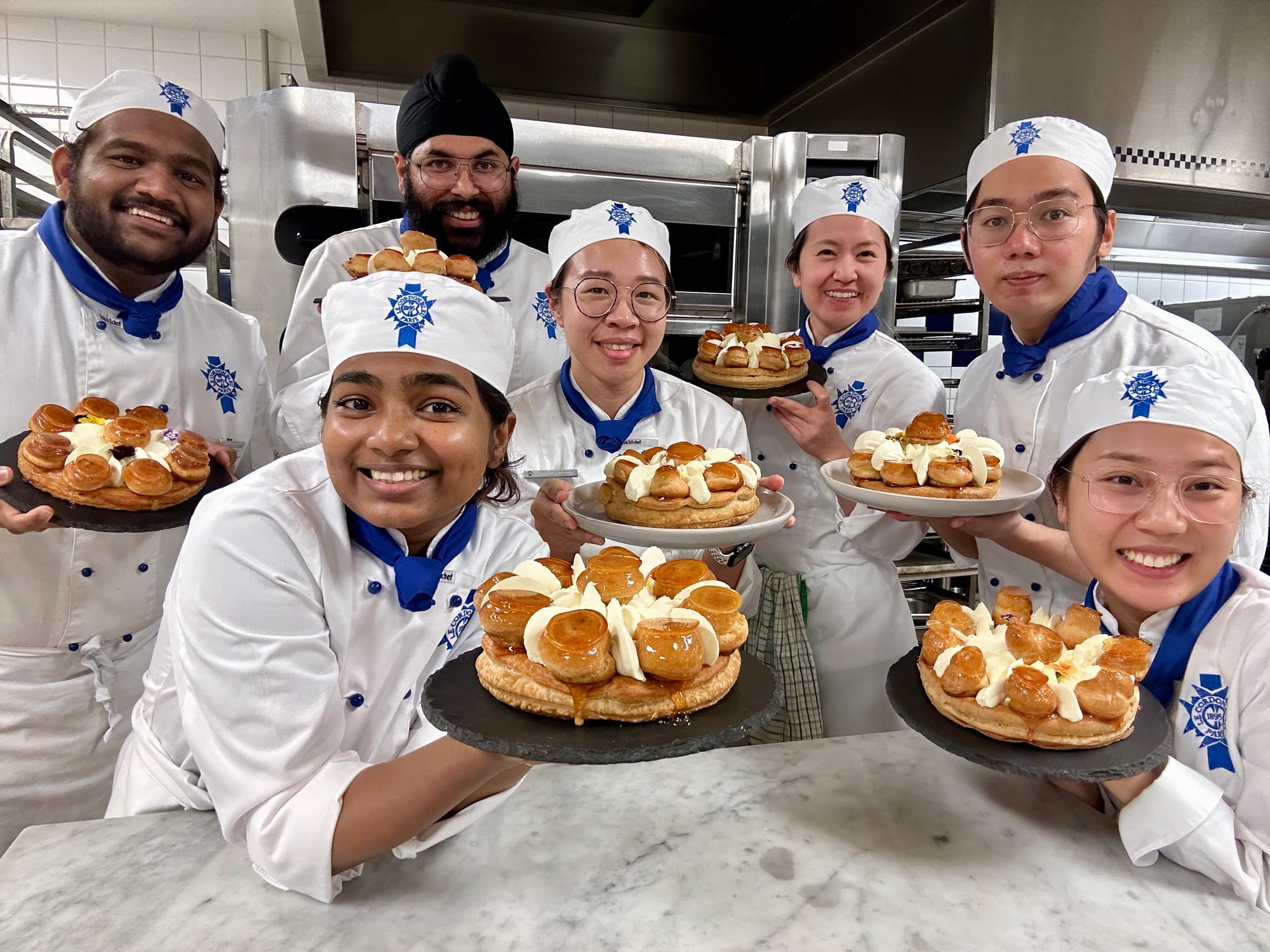 A group of 7 Le Cordon Bleu students in Brisbane Australia holding their pastries up in the kitchen.