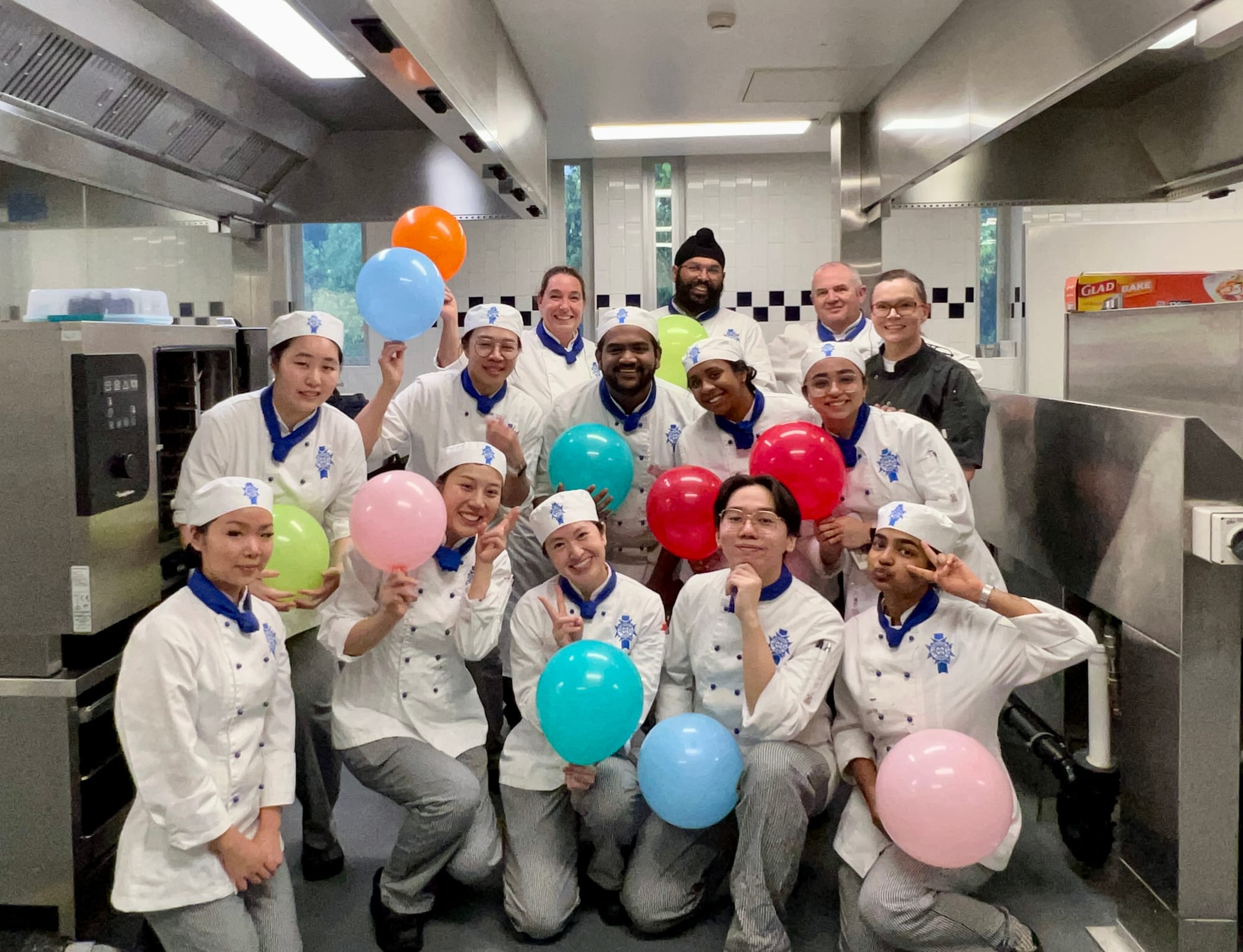 A class photo at a Le Cordon Bleu classroom kitchen in Brisbane Australia. Students are posing with balloons and big smiles.
