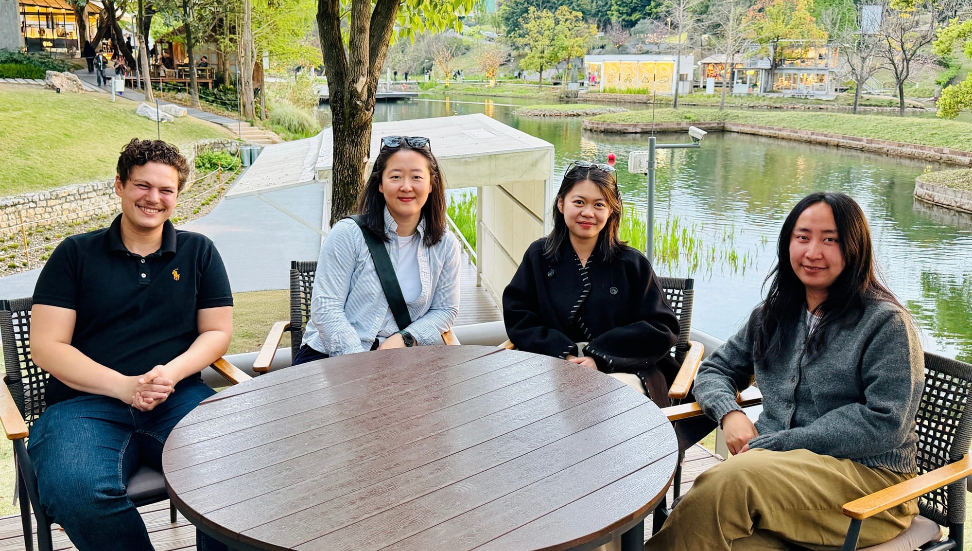 Three Chinese women and a light-skinned Sri Lankan man sitting at a wooden table in front of a pond.