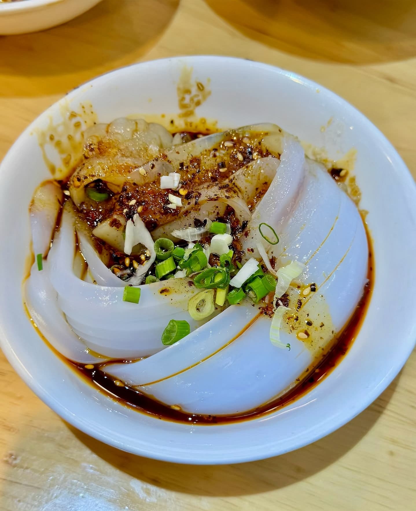 Xuanzi liangfen made from either mung beans or sweet pea. A white bowl with a white noodle-looking material with a mixed red and green sauce.
