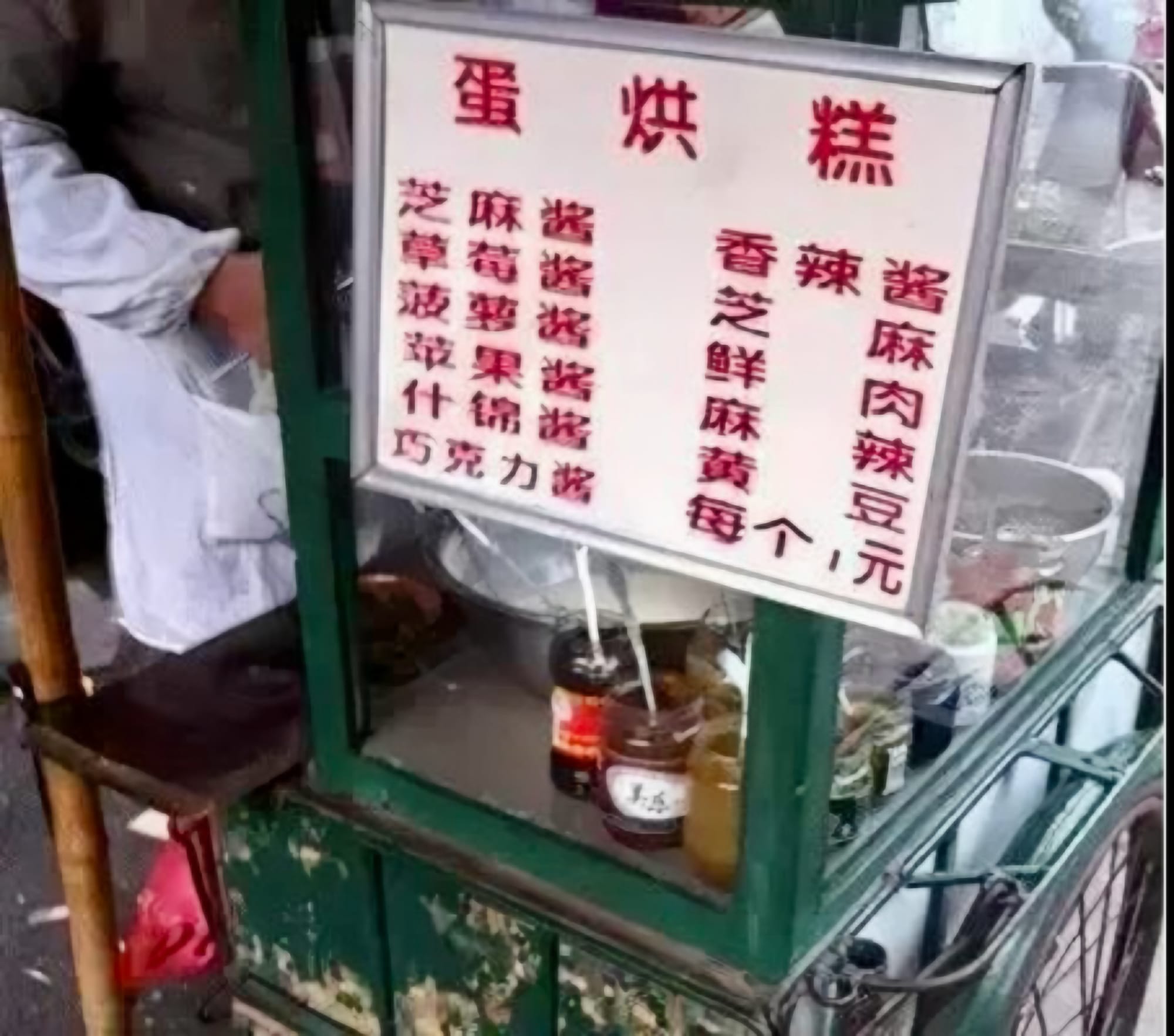 A small street cart with a white sign with red Chinese characters listing the dishes available to be made.