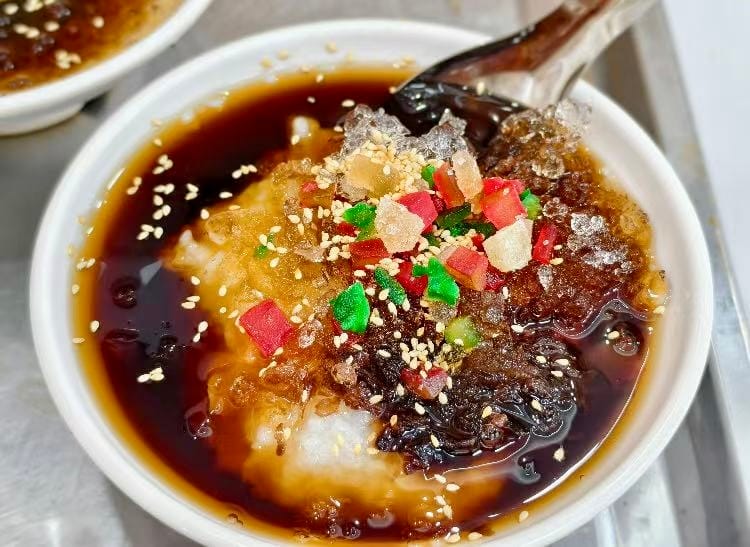 Sweet jelly soup - a clear glass-like looking dessert topped with dried pieces of fruit and brown sugar sauce.