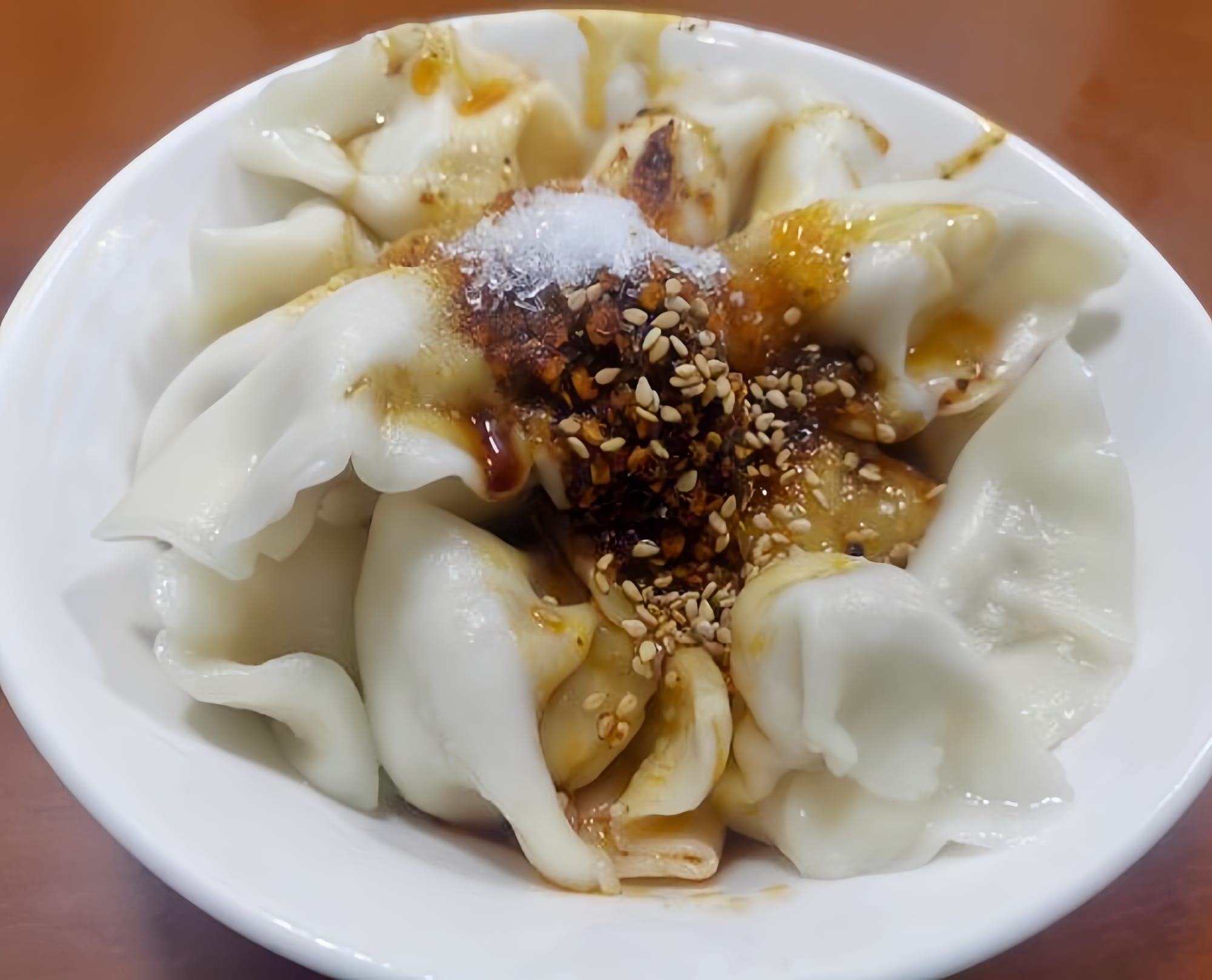 A white bowl of dumplings with a brown sauce with sesame seeds on top.